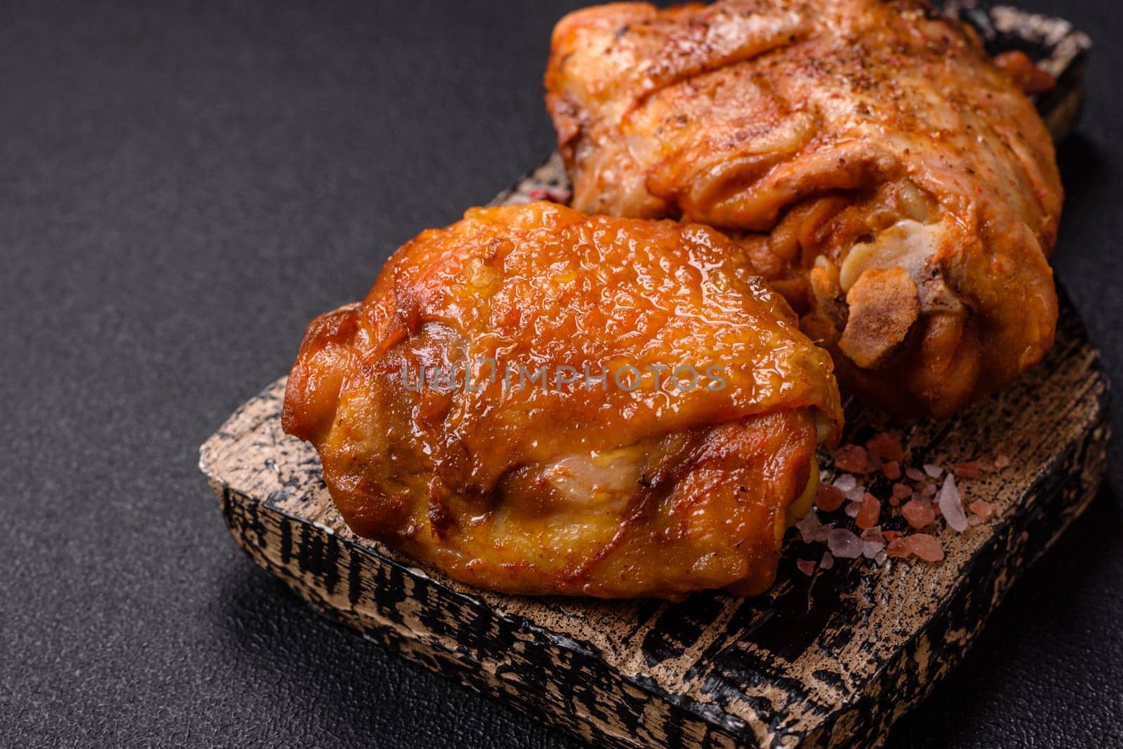 Delicious juicy chicken thighs baked with salt, spices and herbs in a ceramic plate on a dark concrete background