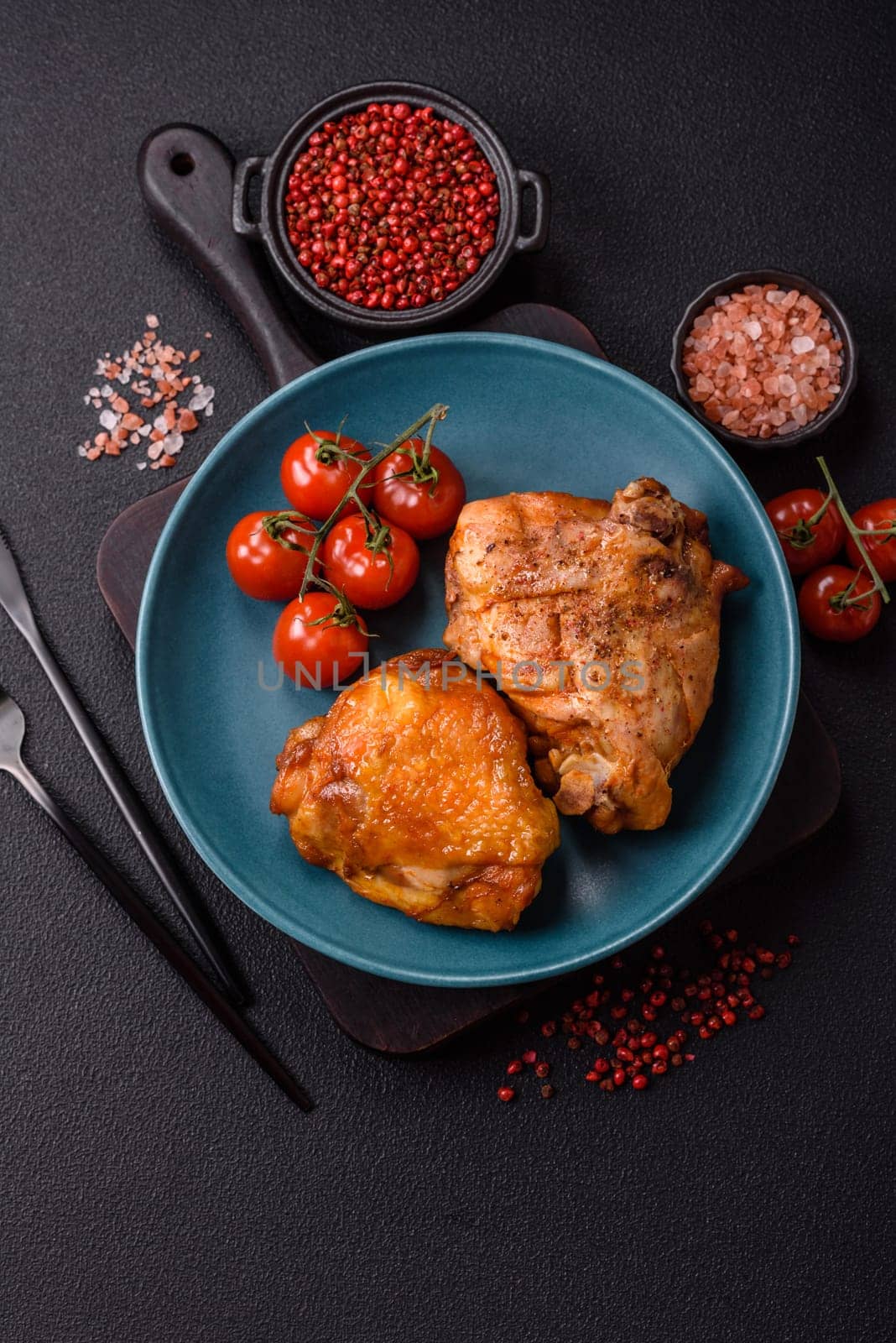 Delicious juicy chicken thighs baked with salt, spices and herbs in a ceramic plate on a dark concrete background