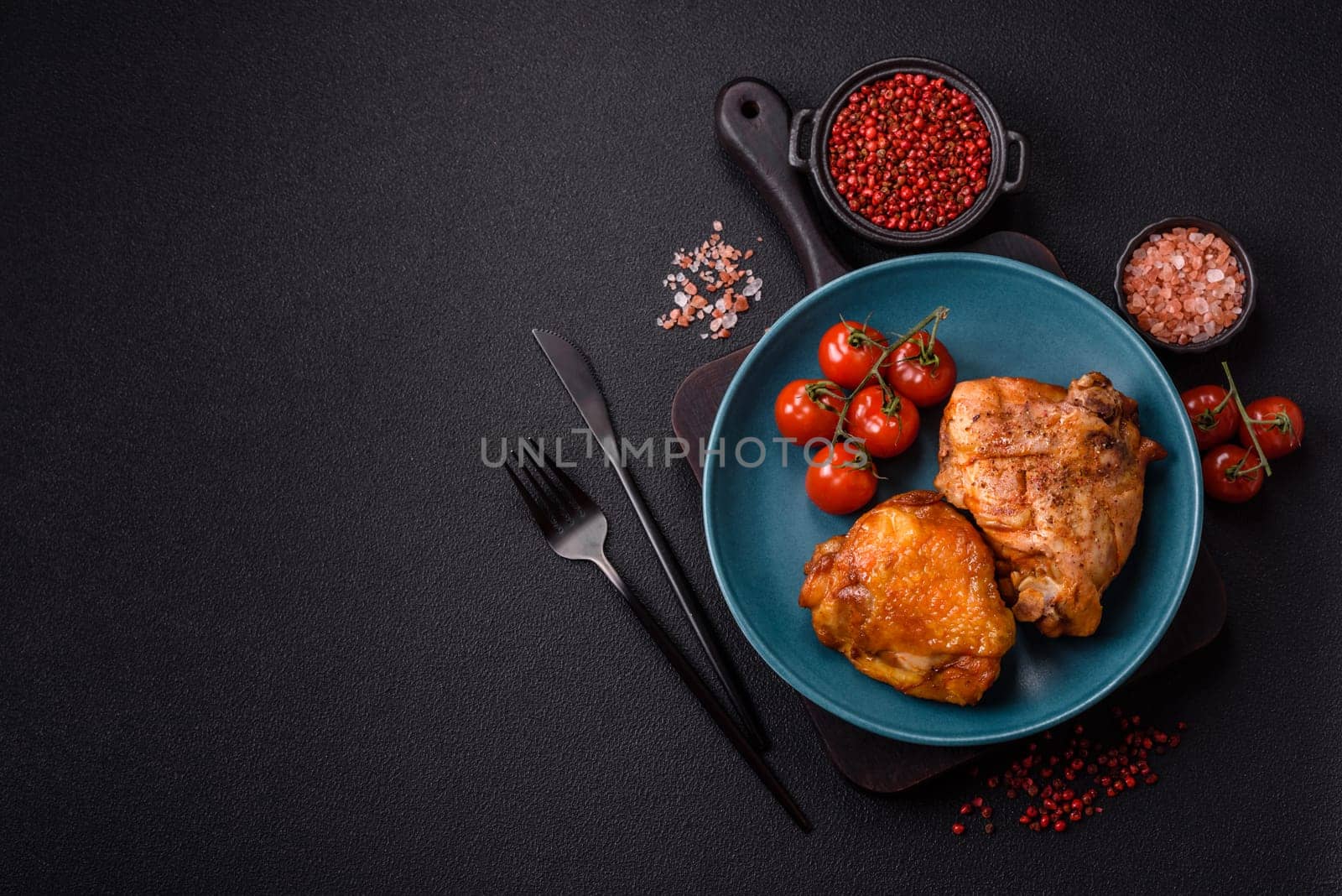 Delicious juicy chicken thighs baked with salt, spices and herbs in a ceramic plate on a dark concrete background