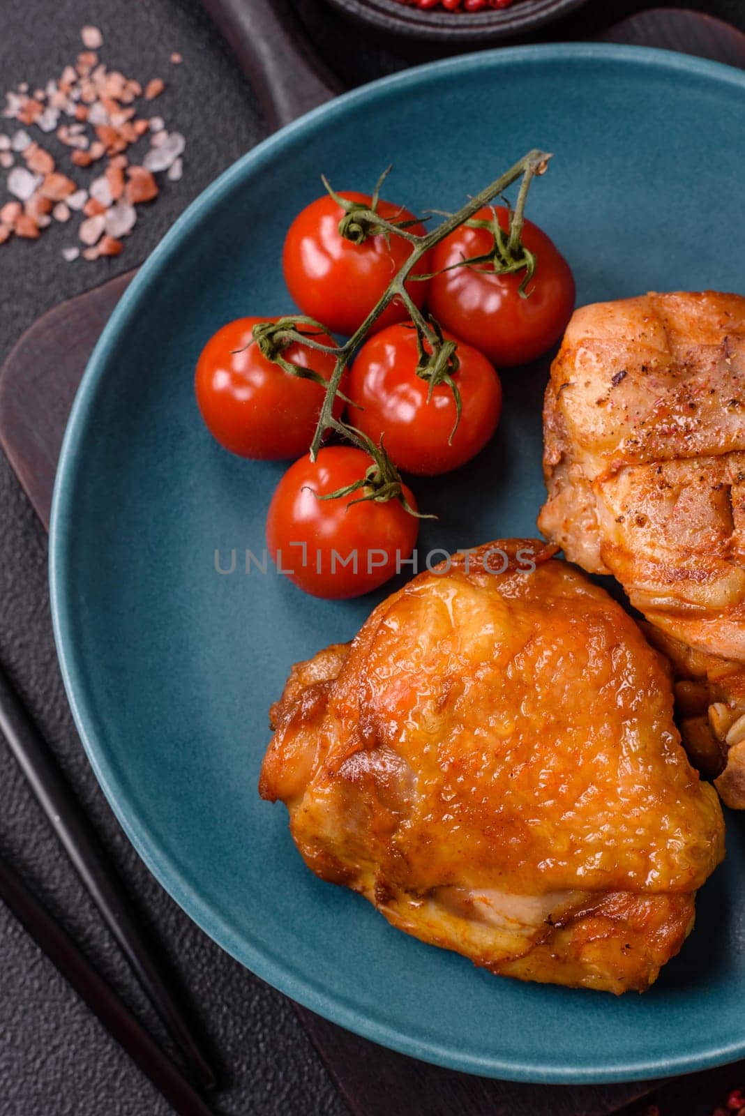 Delicious juicy chicken thighs baked with salt, spices and herbs in a ceramic plate on a dark concrete background