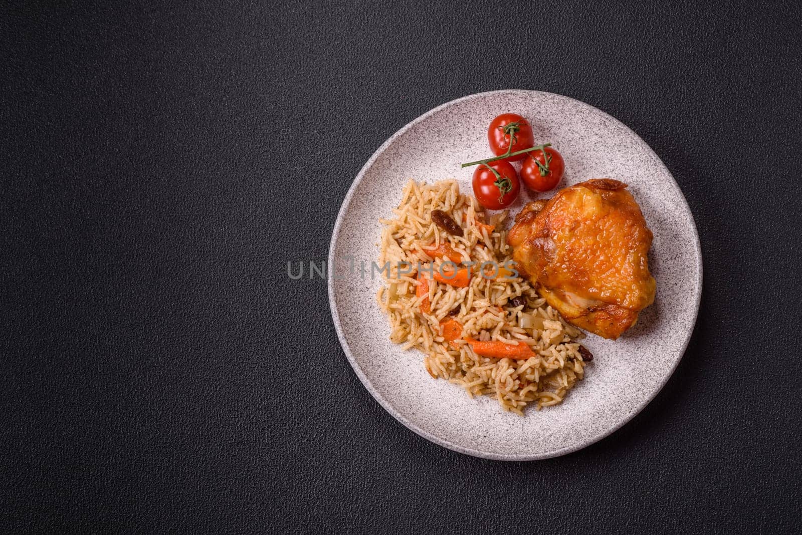 Delicious fresh pilaf with rice, carrots, meat, onions, spices and berries on a ceramic plate on a dark concrete background