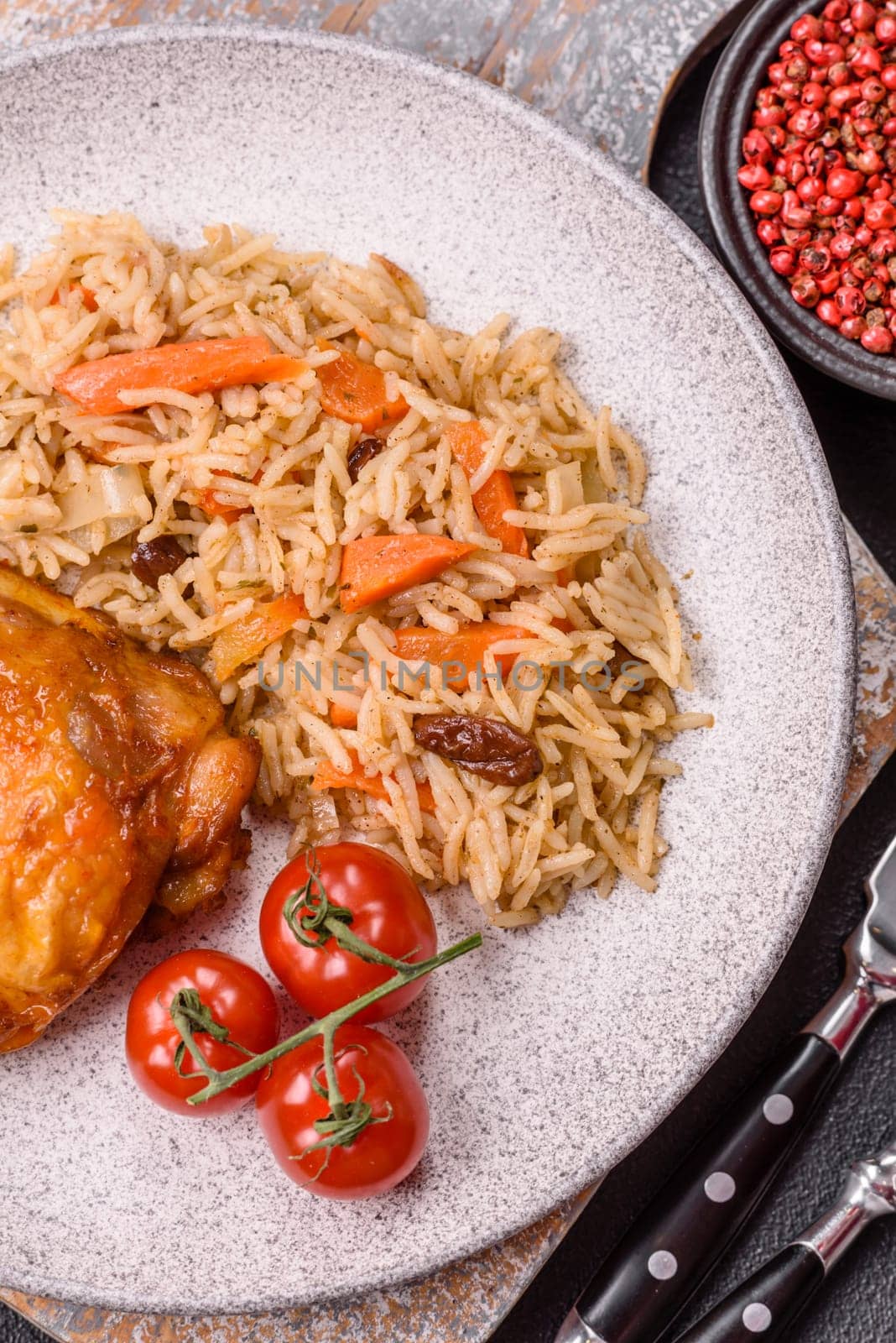 Delicious fresh pilaf with rice, carrots, meat, onions, spices and berries on a ceramic plate on a dark concrete background
