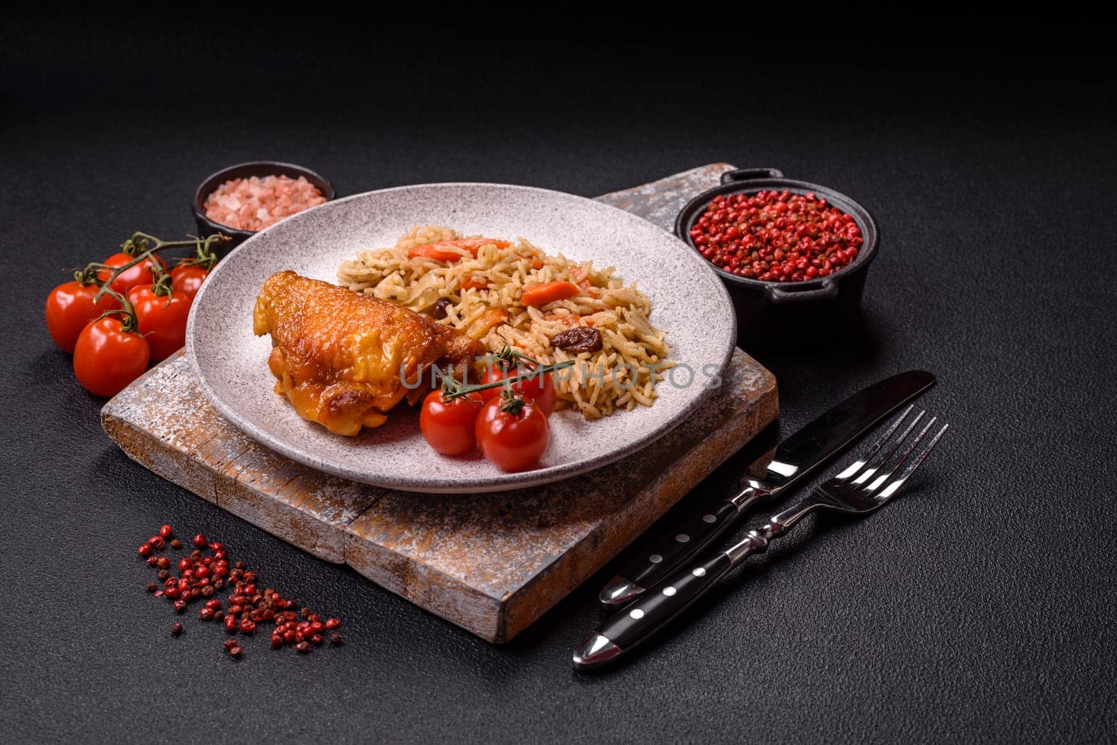 Delicious fresh pilaf with rice, carrots, meat, onions, spices and berries on a ceramic plate on a dark concrete background