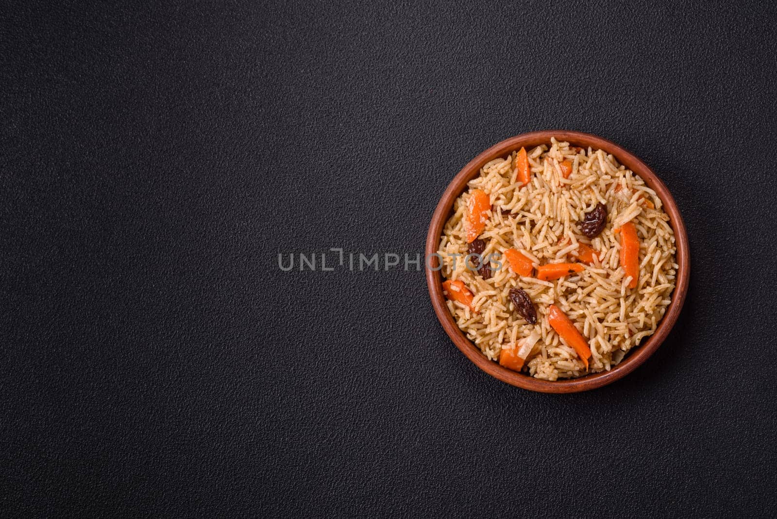 Delicious fresh pilaf with rice, carrots, meat, onions, spices and berries on a ceramic plate on a dark concrete background