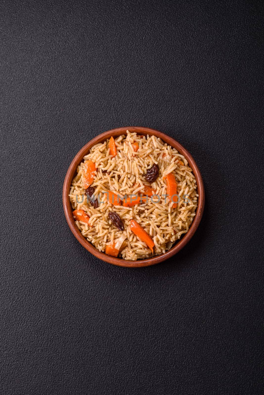 Delicious fresh pilaf with rice, carrots, meat, onions, spices and berries on a ceramic plate on a dark concrete background