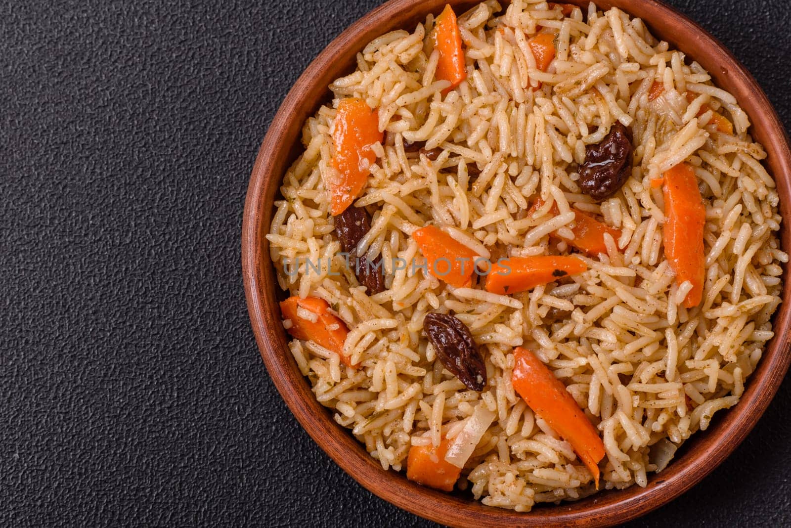 Delicious fresh pilaf with rice, carrots, meat, onions, spices and berries on a ceramic plate on a dark concrete background