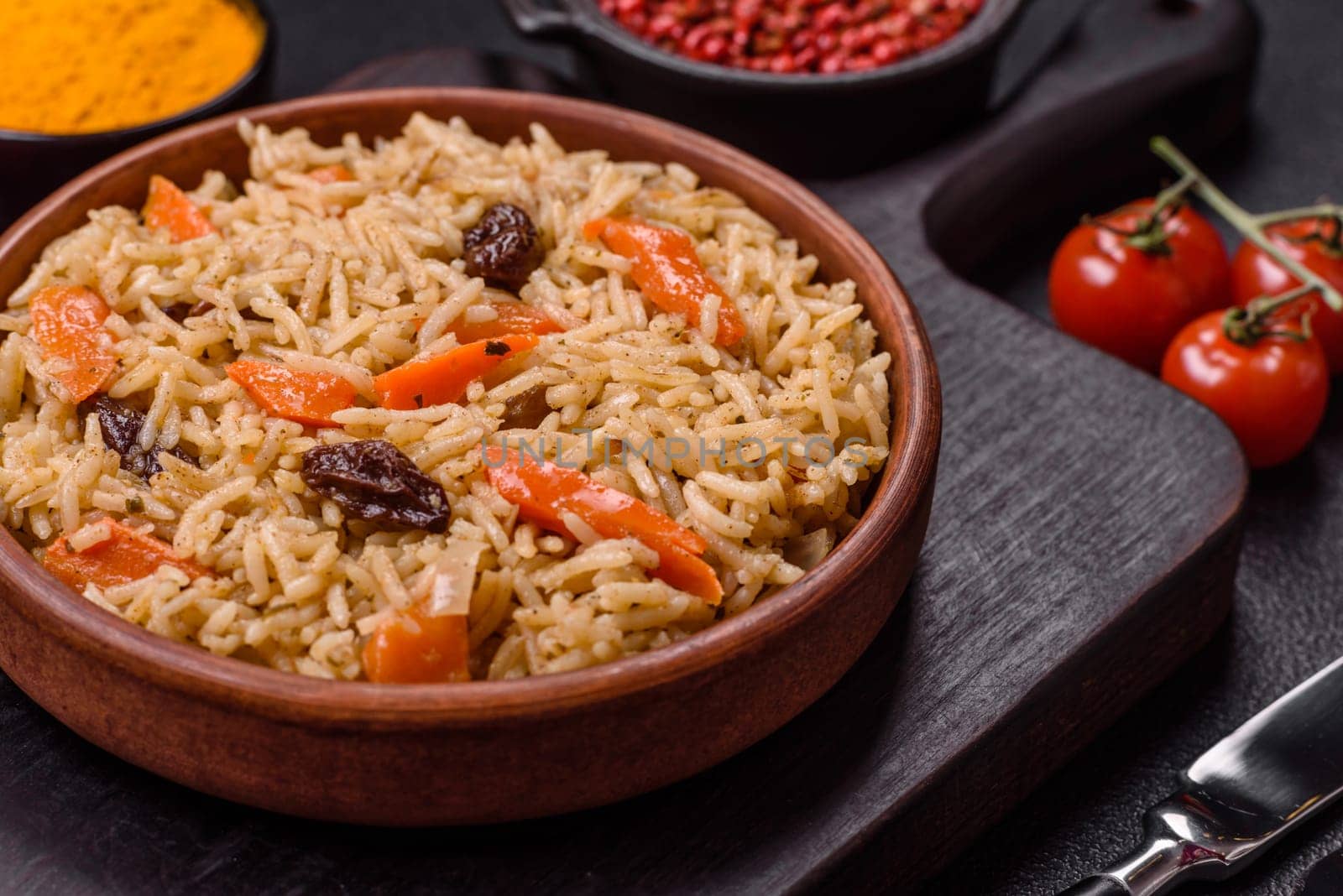 Delicious fresh pilaf with rice, carrots, meat, onions, spices and berries on a ceramic plate on a dark concrete background