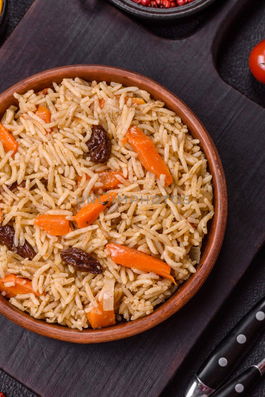 Delicious fresh pilaf with rice, carrots, meat, onions, spices and berries on a ceramic plate on a dark concrete background