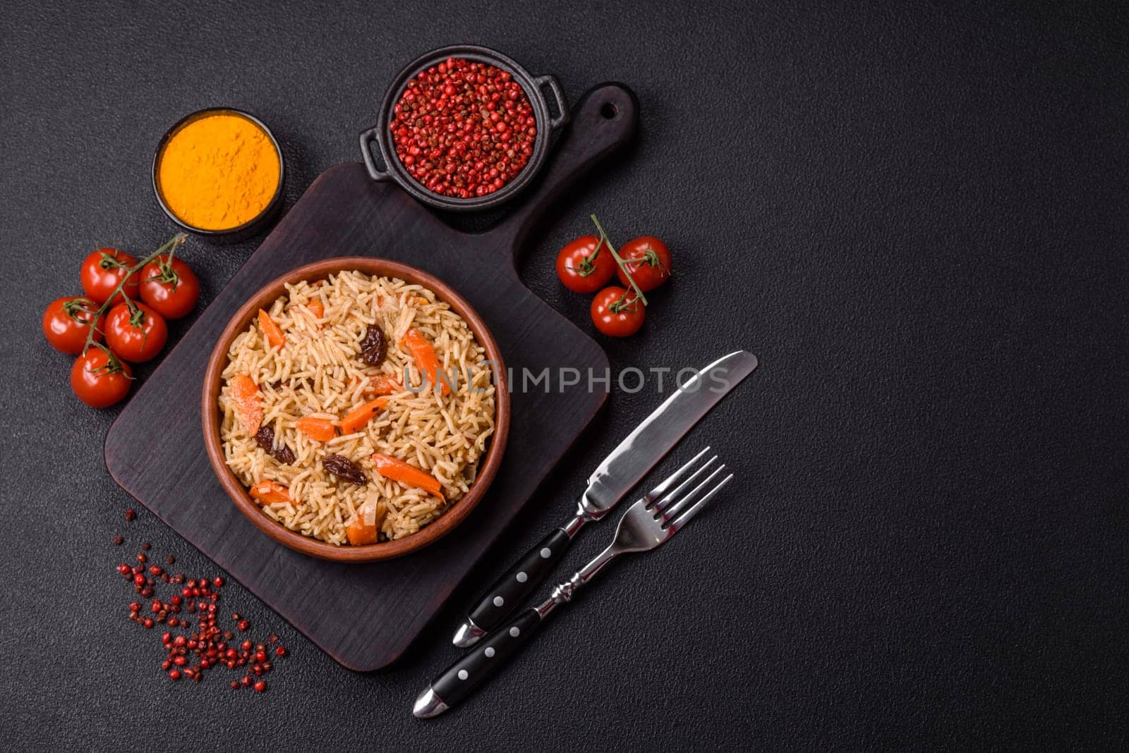 Delicious fresh pilaf with rice, carrots, meat, onions, spices and berries on a ceramic plate on a dark concrete background