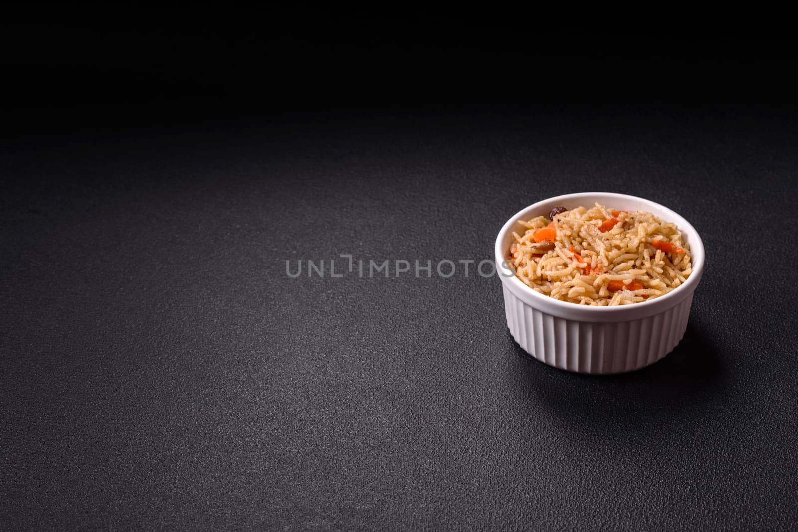 Delicious fresh pilaf with rice, carrots, meat, onions, spices and berries on a ceramic plate on a dark concrete background