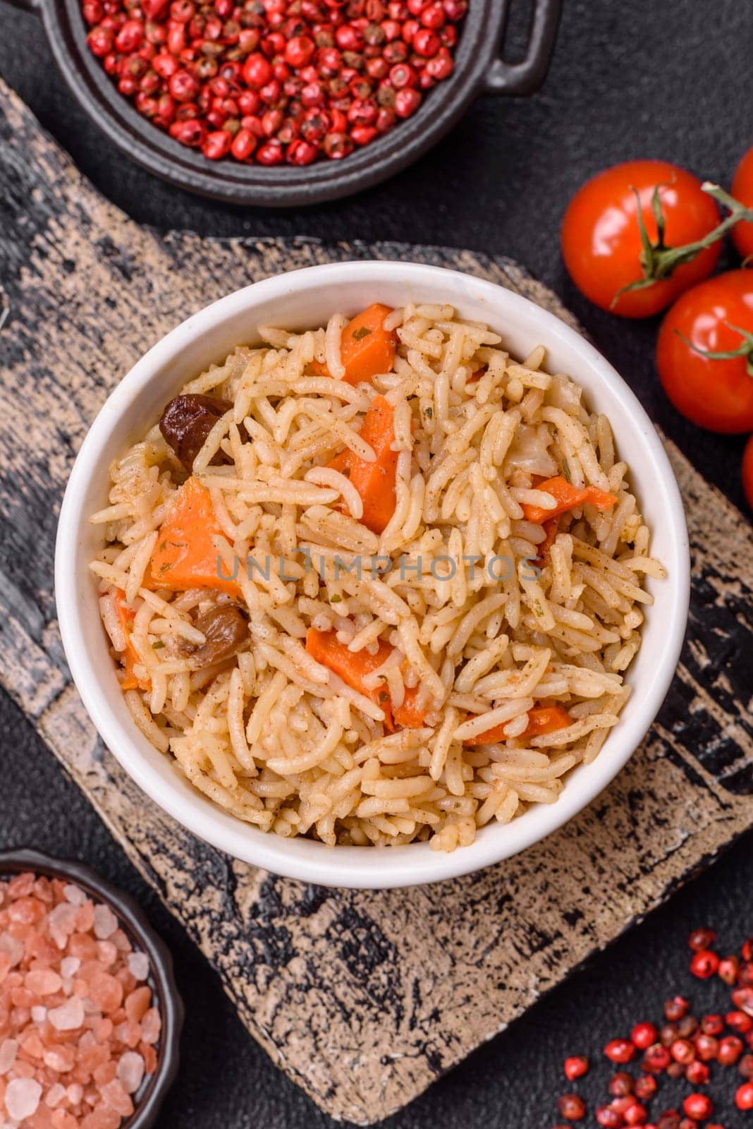 Delicious fresh pilaf with rice, carrots, meat, onions, spices and berries on a ceramic plate on a dark concrete background