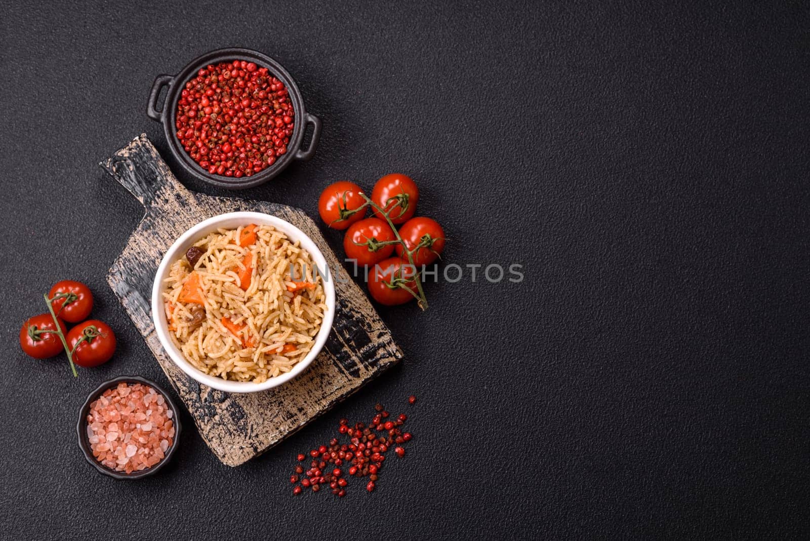 Delicious fresh pilaf with rice, carrots, meat, onions, spices and berries on a ceramic plate on a dark concrete background