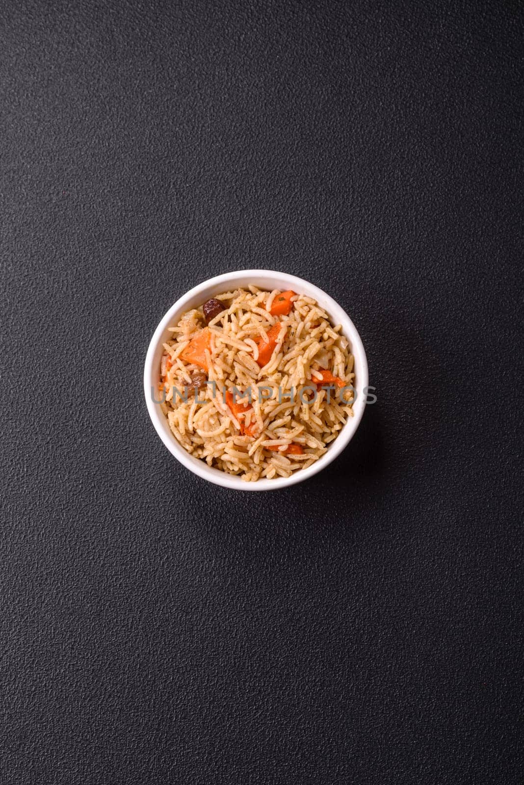 Delicious fresh pilaf with rice, carrots, meat, onions, spices and berries on a ceramic plate on a dark concrete background