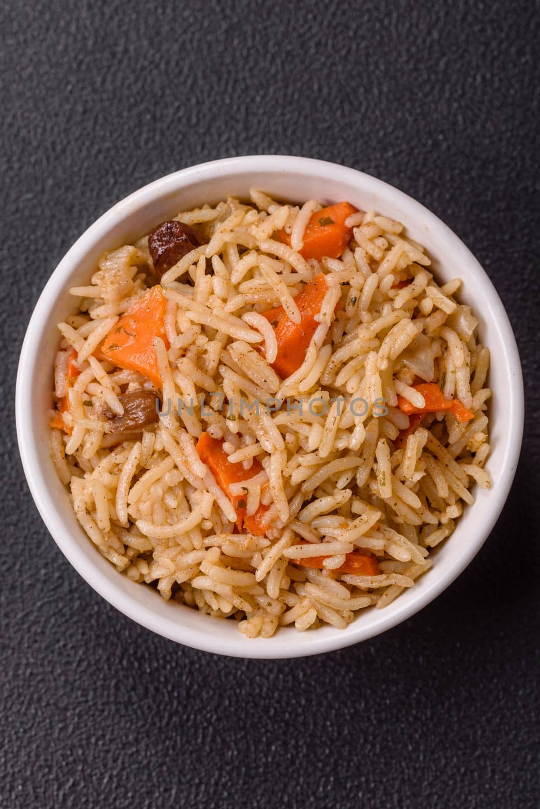 Delicious fresh pilaf with rice, carrots, meat, onions, spices and berries on a ceramic plate on a dark concrete background