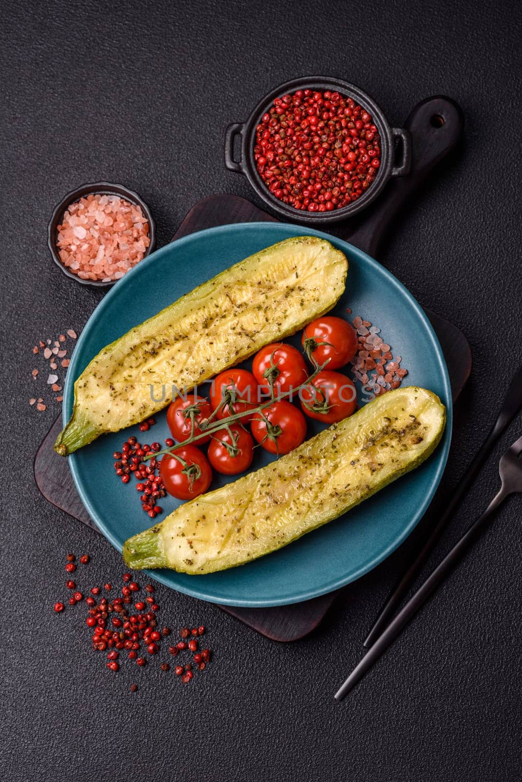 Delicious zucchini cut into two halves baked with salt, spices and herbs on a dark concrete background