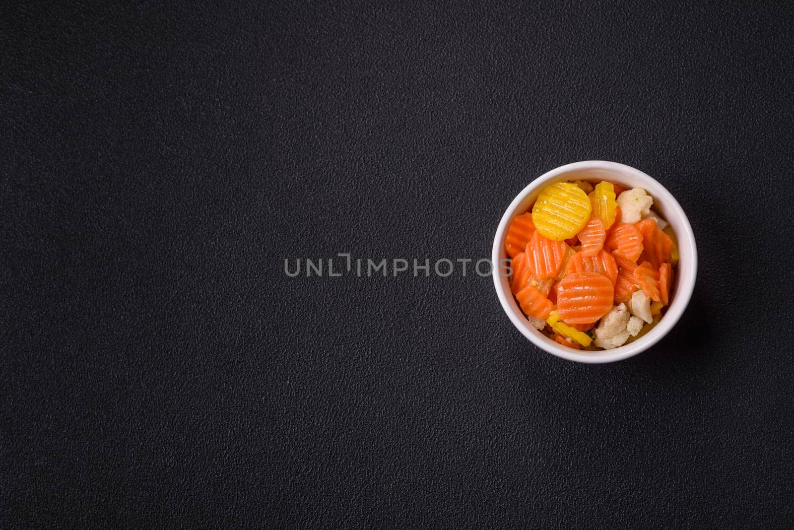 Delicious fresh vegetables steamed carrots, broccoli, cauliflower on a black plate on a dark concrete background
