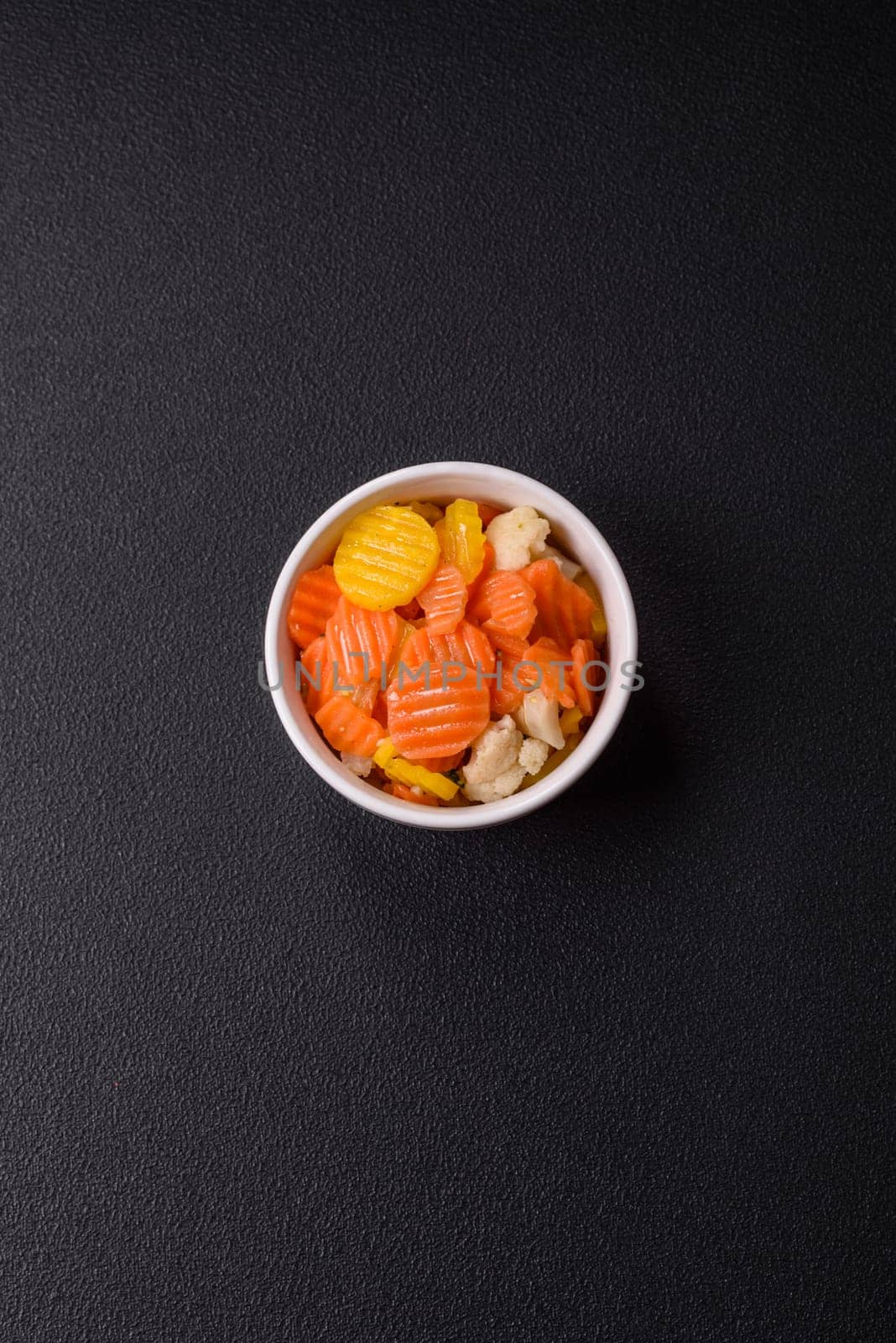 Delicious fresh vegetables steamed carrots, broccoli, cauliflower on a black plate on a dark concrete background