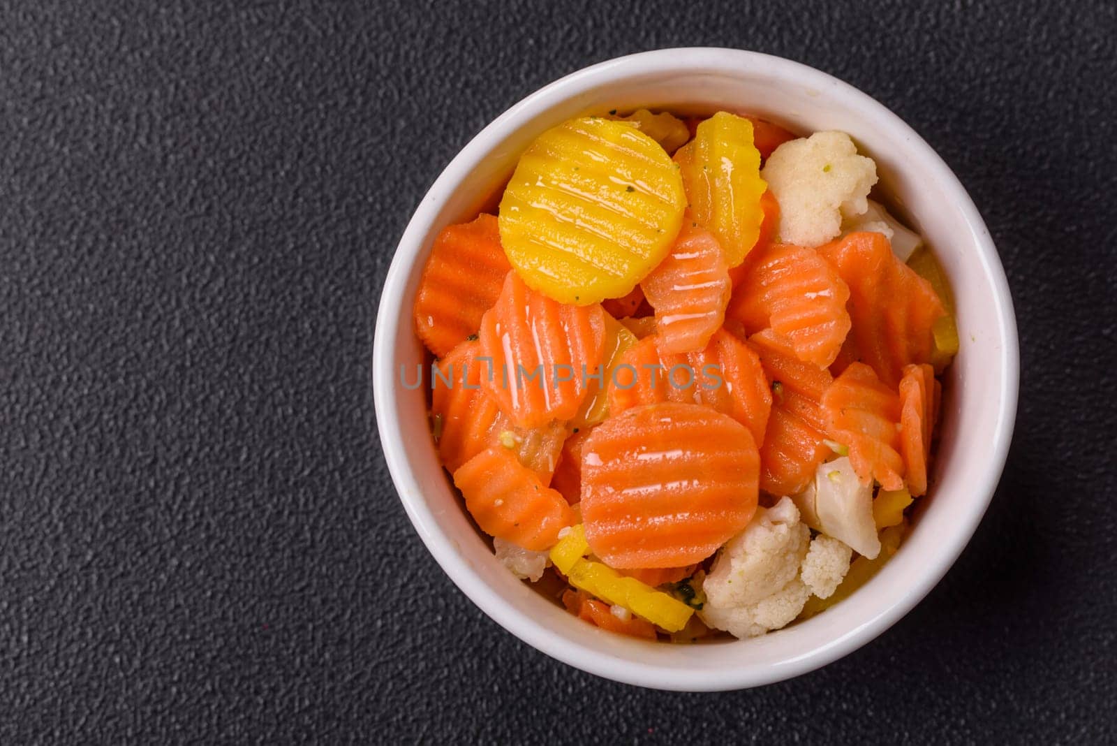 Delicious fresh vegetables steamed carrots, broccoli, cauliflower on a black plate on a dark concrete background
