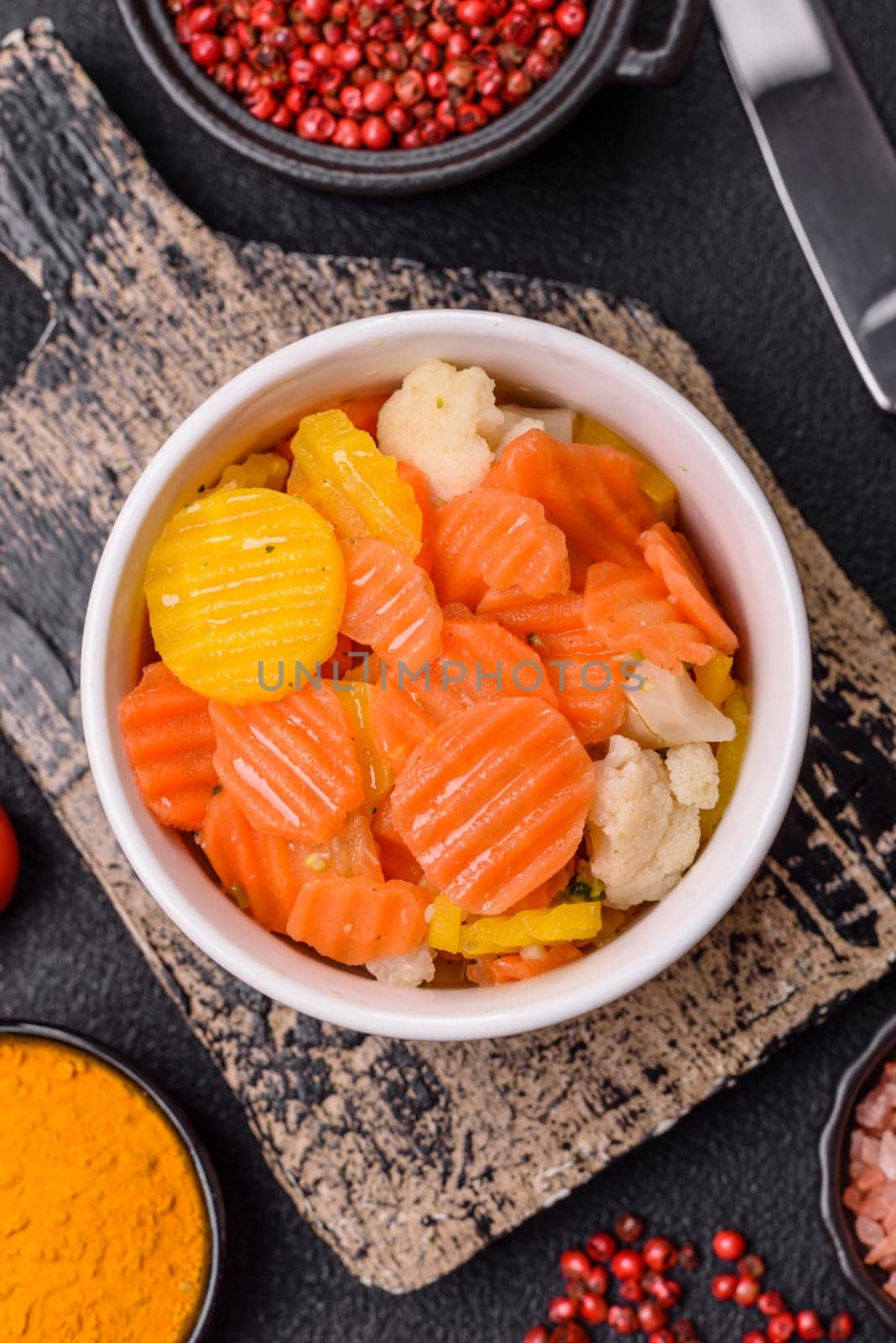 Delicious fresh vegetables steamed carrots, broccoli, cauliflower on a black plate on a dark concrete background
