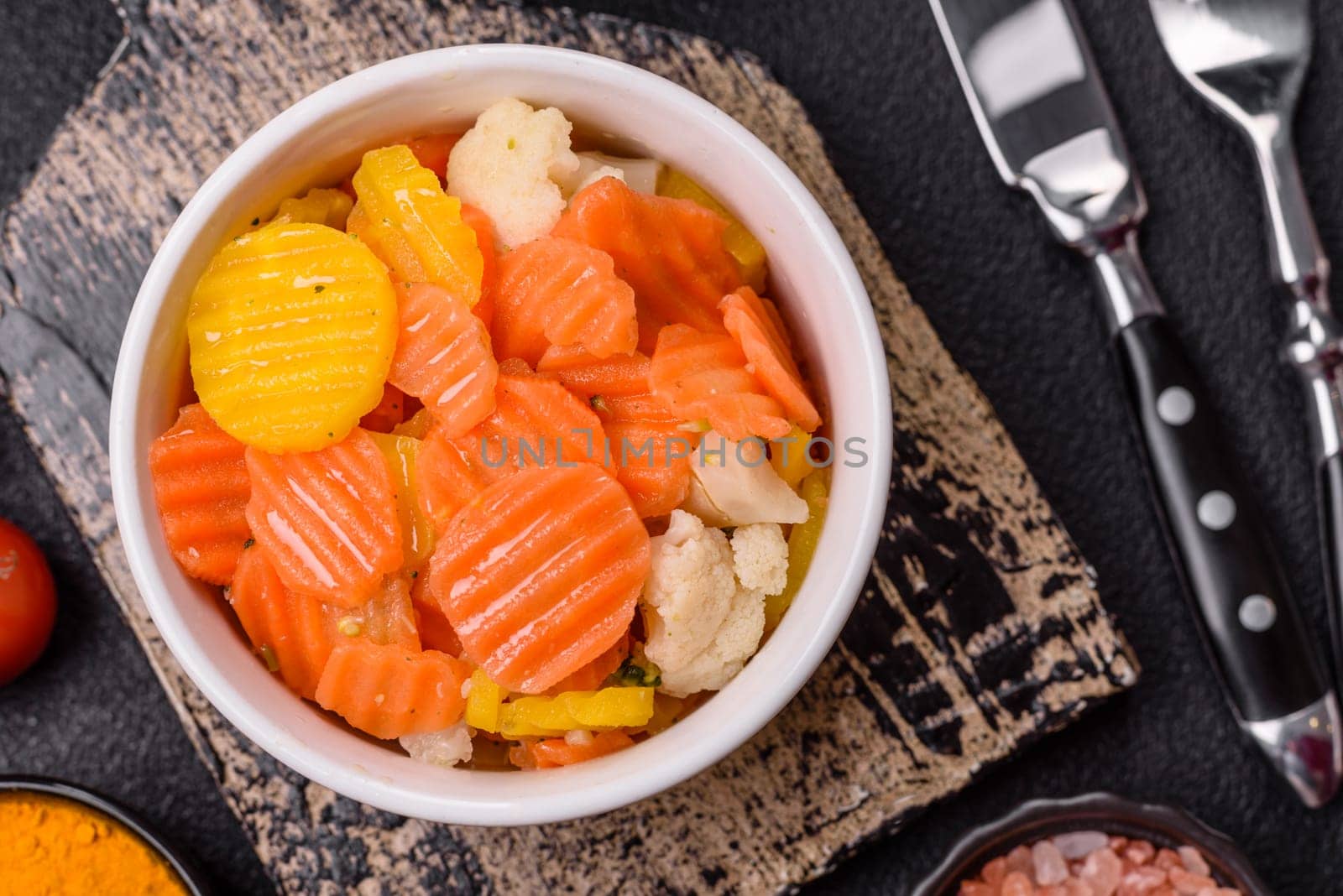 Delicious fresh vegetables steamed carrots, broccoli, cauliflower on a black plate on a dark concrete background
