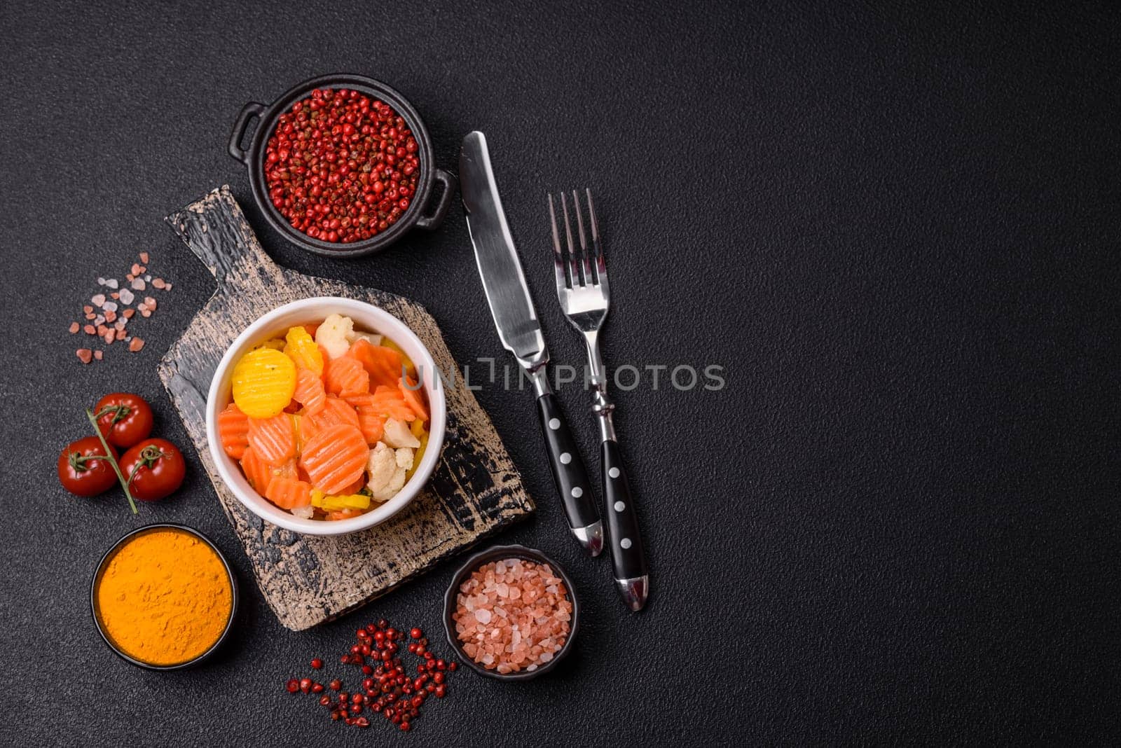 Delicious fresh vegetables steamed carrots, broccoli, cauliflower on a black plate on a dark concrete background