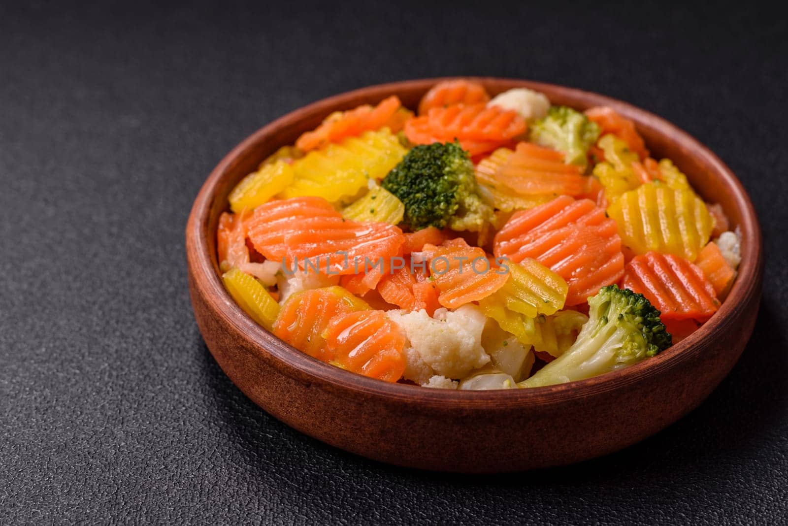 Delicious fresh vegetables steamed carrots, broccoli, cauliflower on a black plate on a dark concrete background