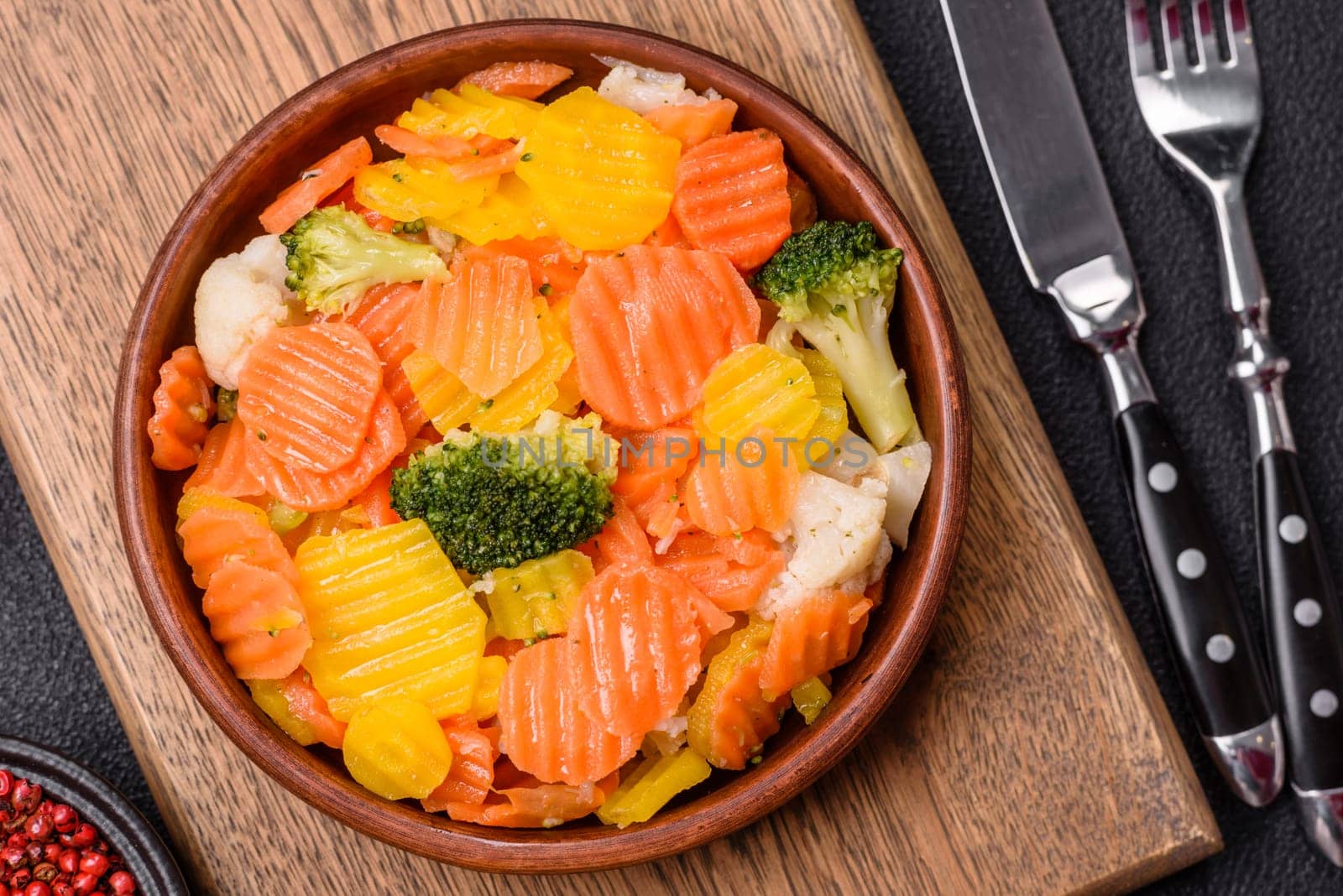 Delicious fresh vegetables steamed carrots, broccoli, cauliflower on a black plate on a dark concrete background