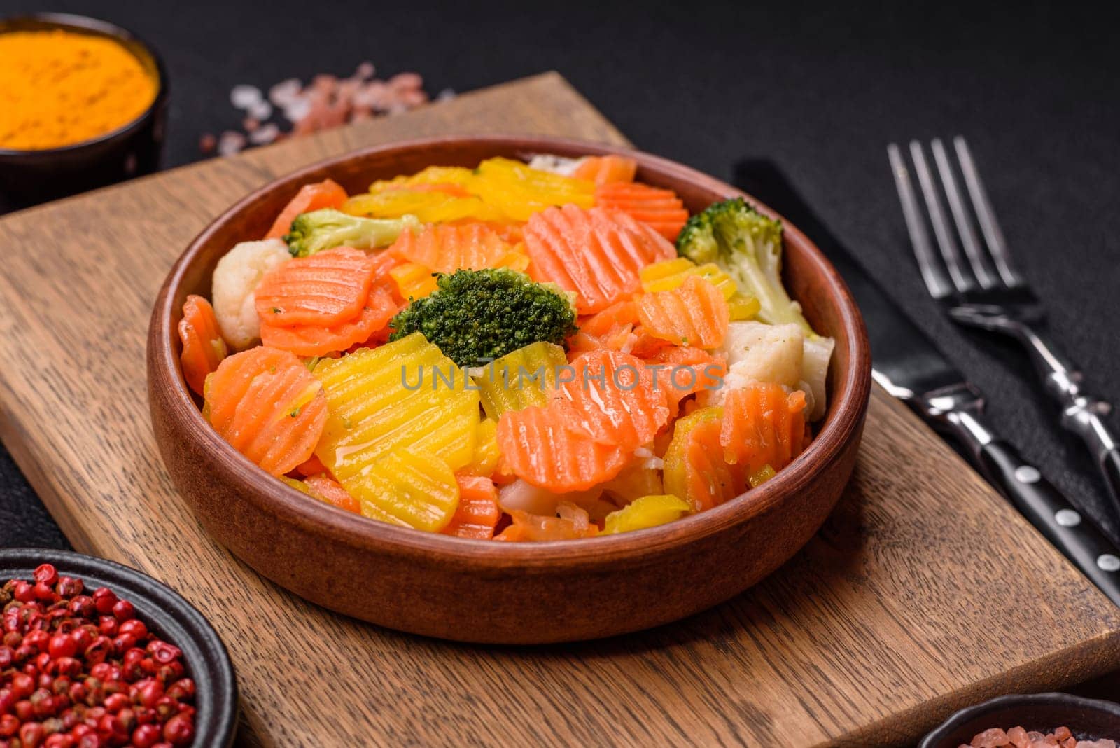 Delicious fresh vegetables steamed carrots, broccoli, cauliflower on a black plate on a dark concrete background