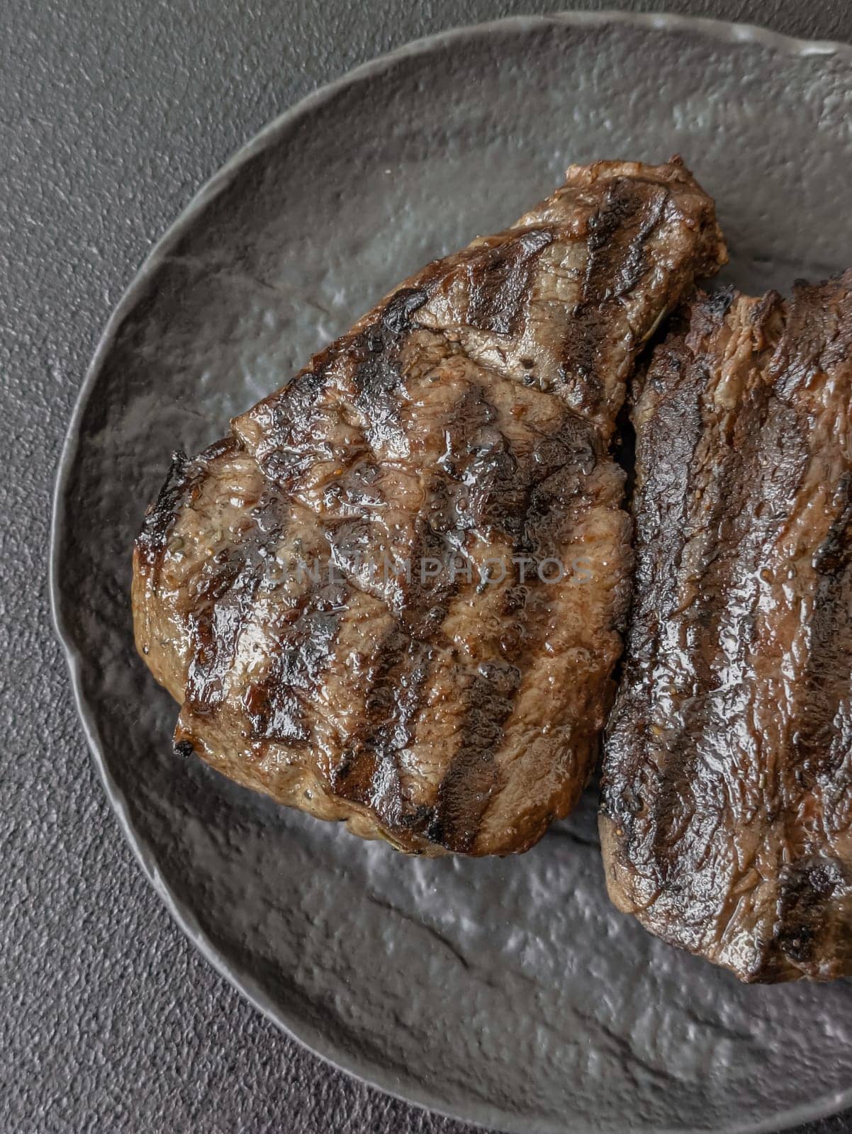 Grilled beef steak with salt, spices and herbs on dark concrete background