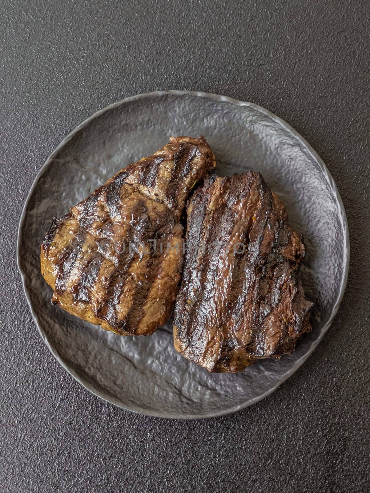 Grilled beef steak with salt, spices and herbs on dark concrete background
