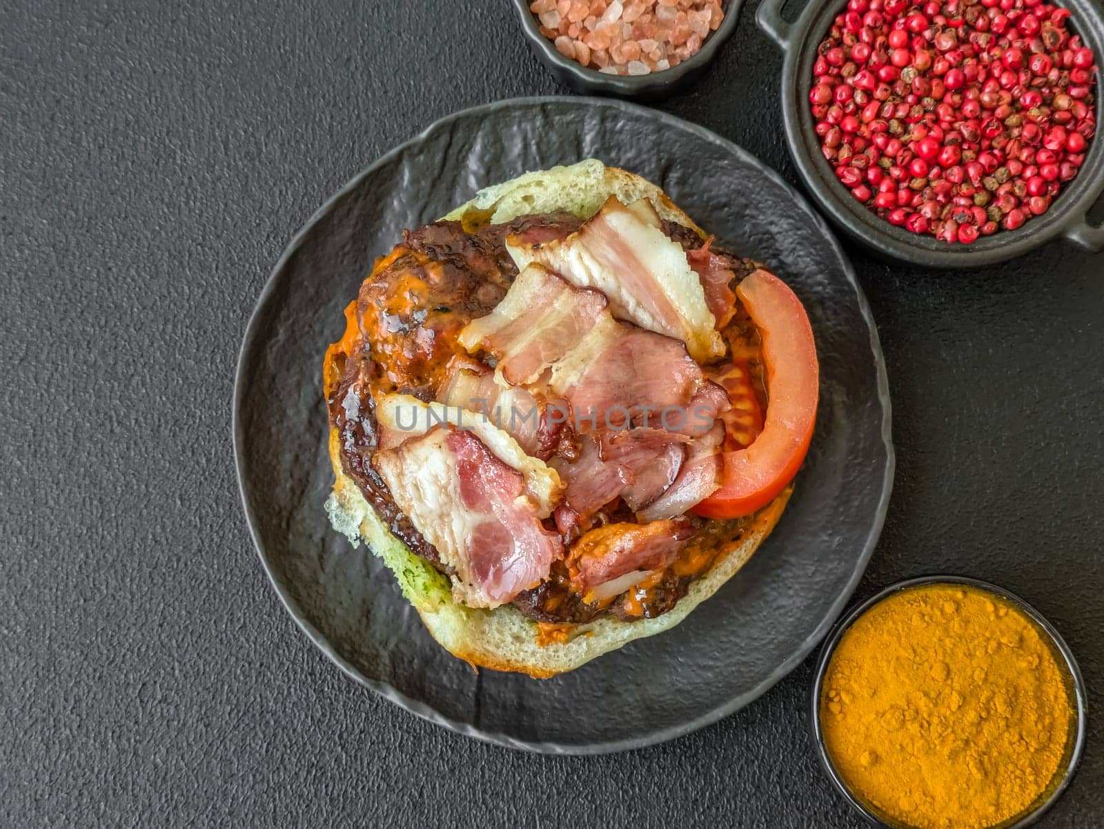 Juicy burger with beef patty, tomatoes, cheese, bacon, salt and spices on dark concrete background
