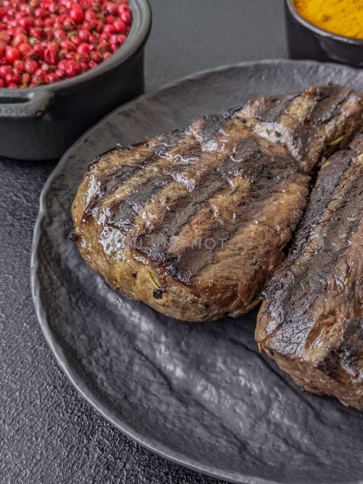 Grilled beef steak with salt, spices and herbs on dark concrete background