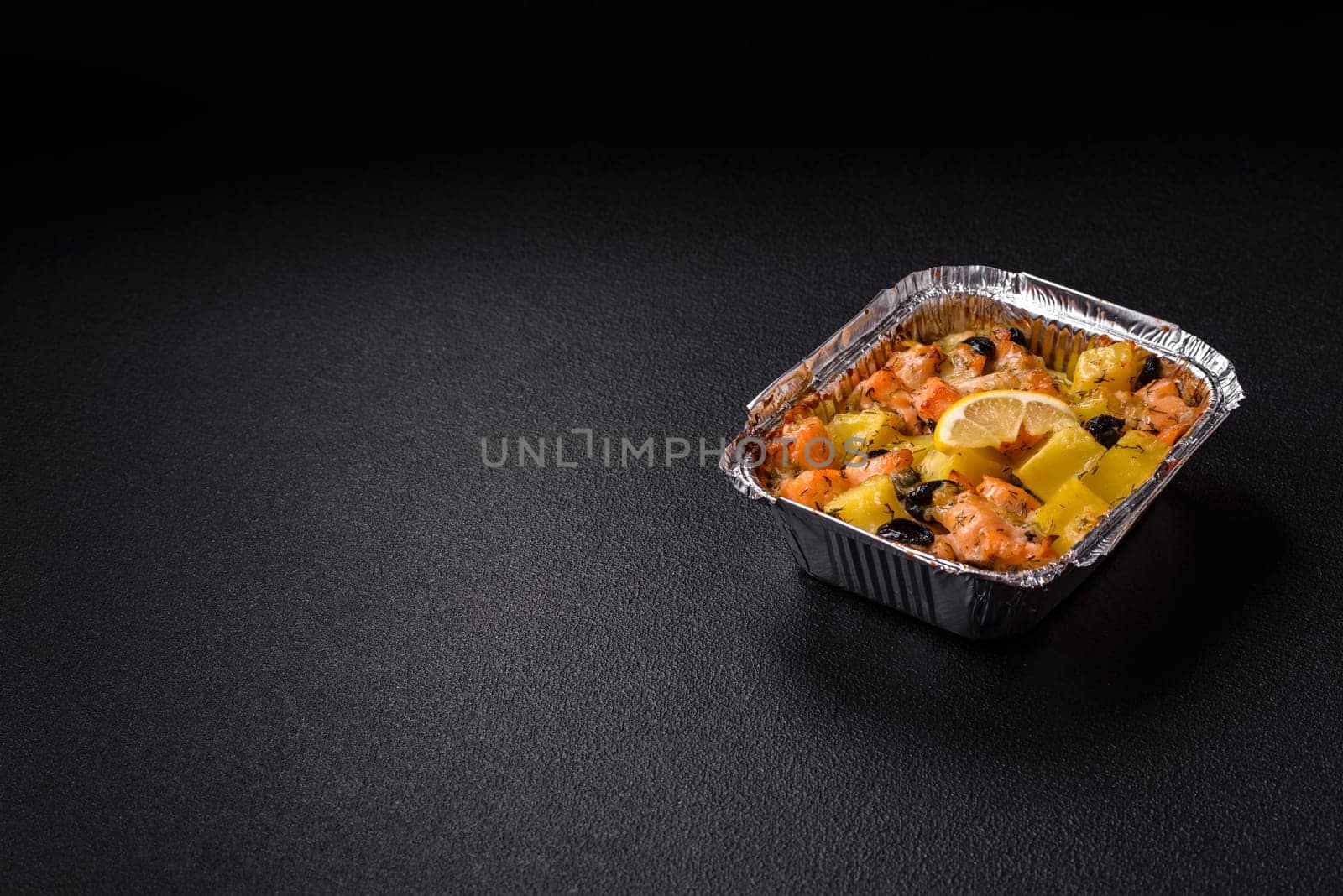 Baked salmon pieces with potatoes, cheese and olives with salt, spices and herbs on a dark concrete background