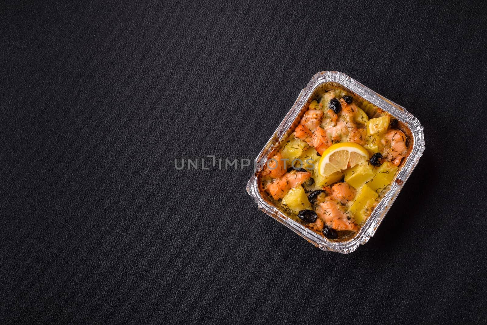 Baked salmon pieces with potatoes, cheese and olives with salt, spices and herbs on a dark concrete background