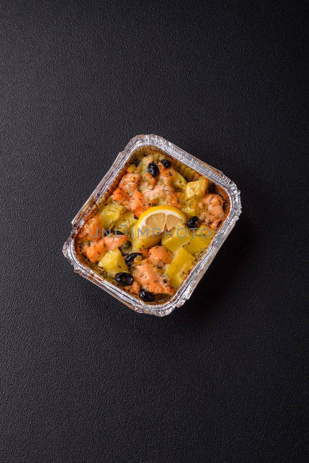 Baked salmon pieces with potatoes, cheese and olives with salt, spices and herbs on a dark concrete background
