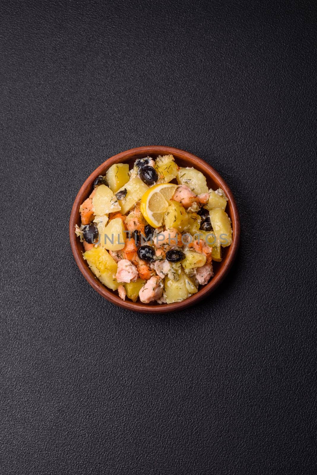 Baked salmon pieces with potatoes, cheese and olives with salt, spices and herbs on a dark concrete background