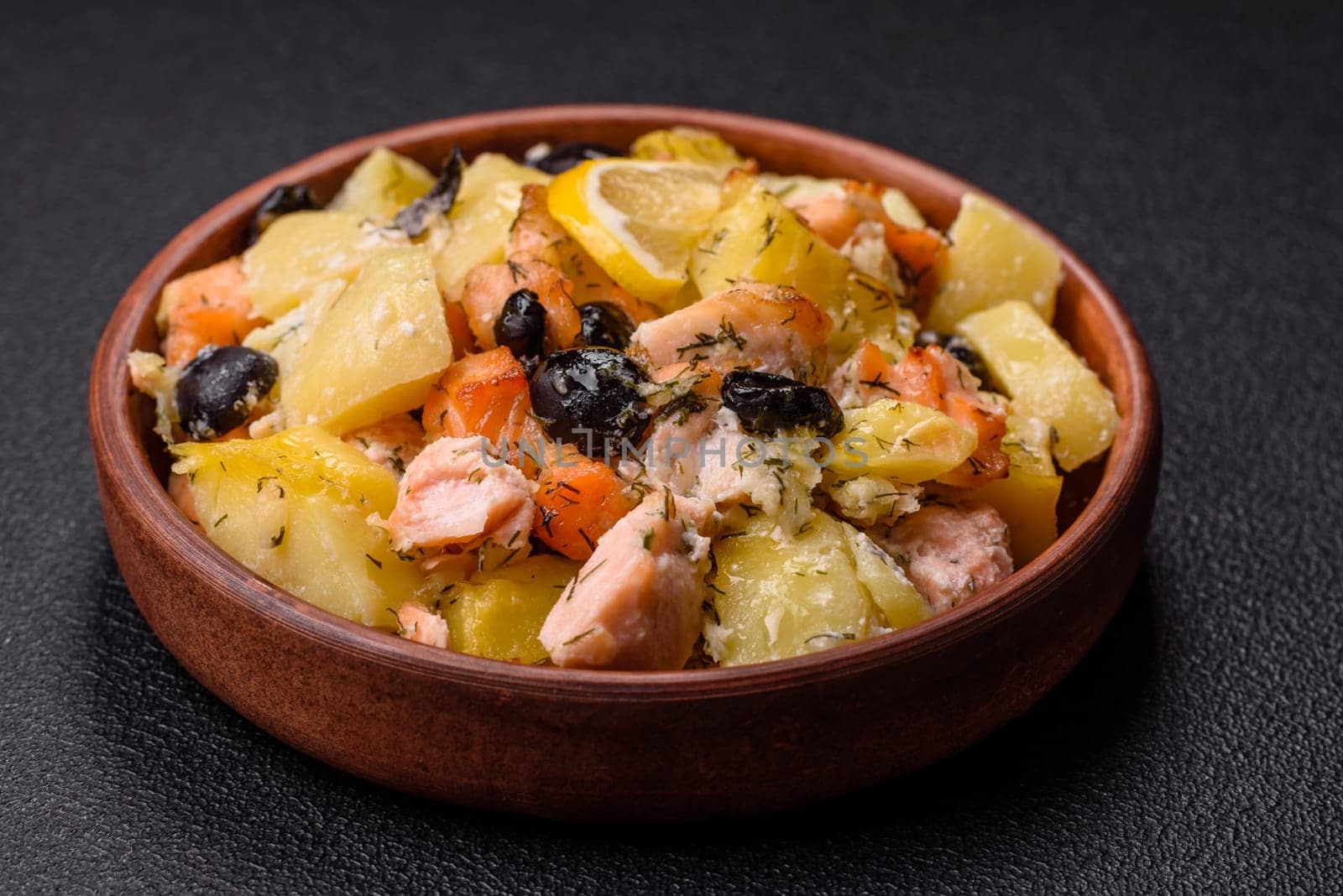 Baked salmon pieces with potatoes, cheese and olives with salt, spices and herbs on a dark concrete background