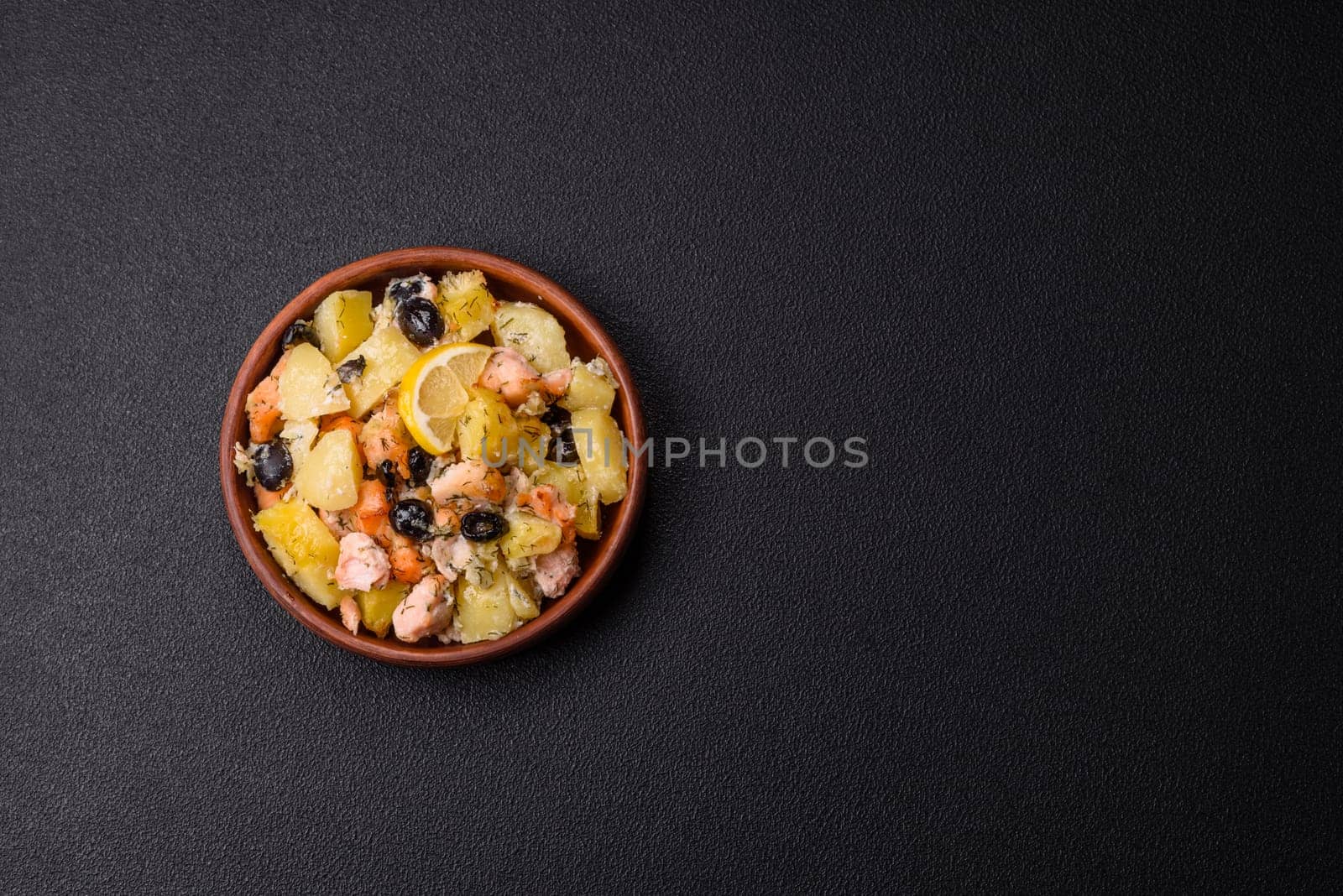 Baked salmon pieces with potatoes, cheese and olives with salt, spices and herbs on a dark concrete background