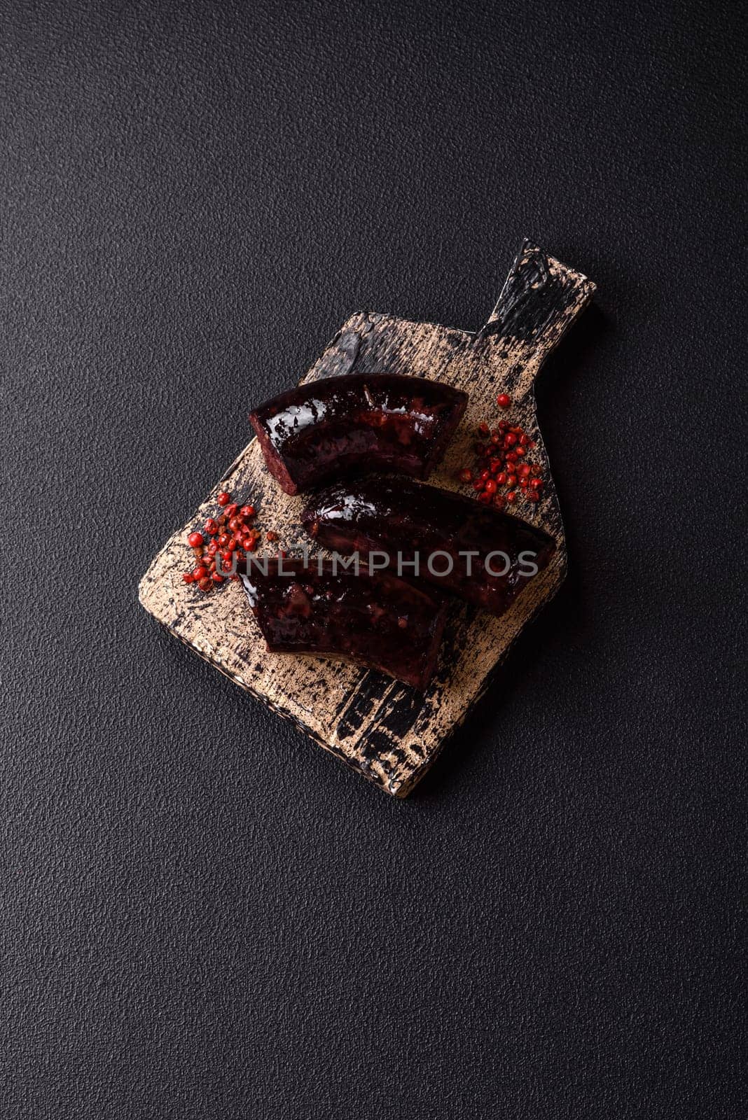 Delicious black blood sausage or black pudding with spices and herbs grilled on a black concrete background