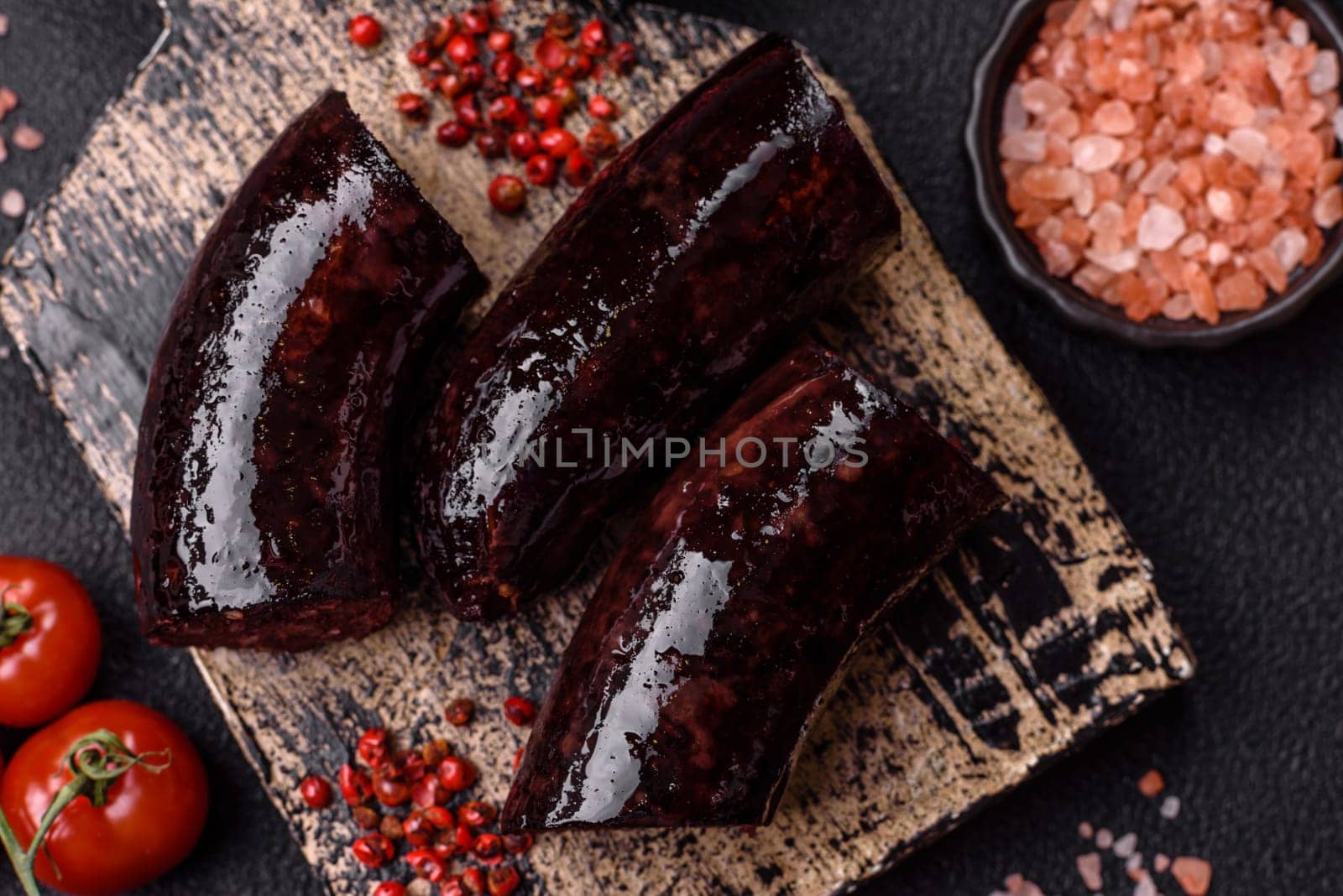 Delicious black blood sausage or black pudding with spices and herbs grilled on a black concrete background