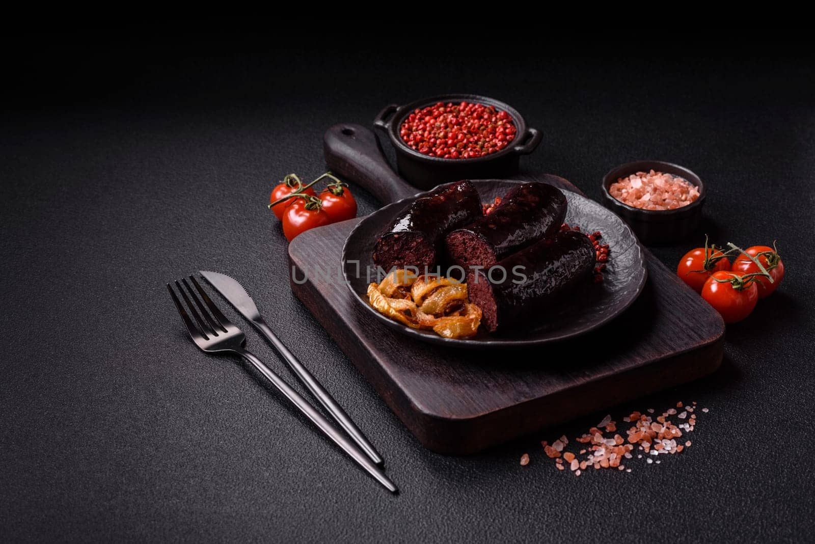 Delicious black blood sausage or black pudding with spices and herbs grilled on a black concrete background