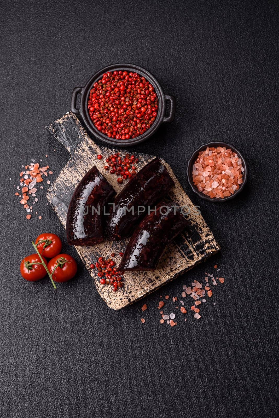 Delicious black blood sausage or black pudding with spices and herbs grilled on a black concrete background