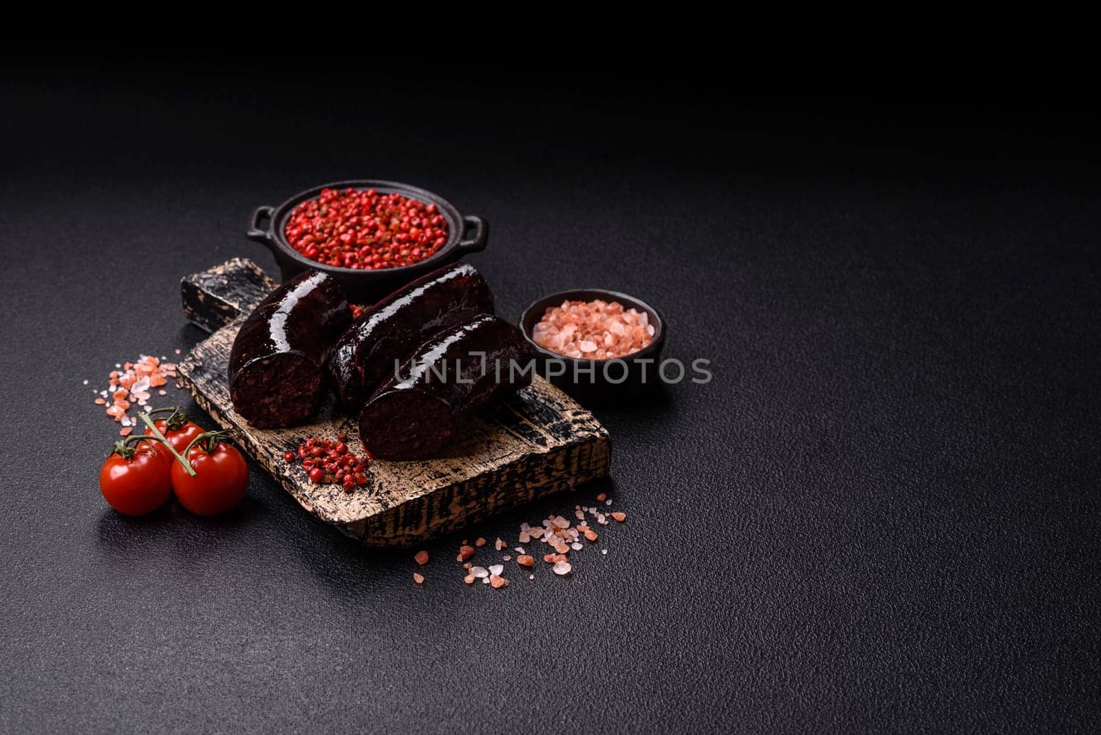 Delicious black blood sausage or black pudding with spices and herbs grilled on a black concrete background