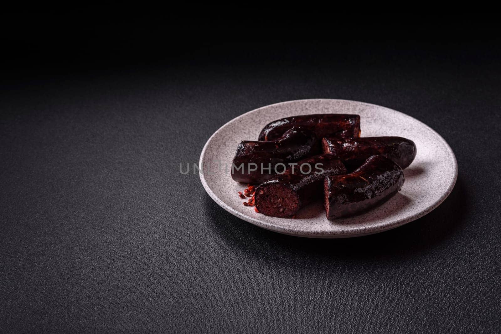 Delicious black blood sausage or black pudding with spices and herbs grilled on a black concrete background