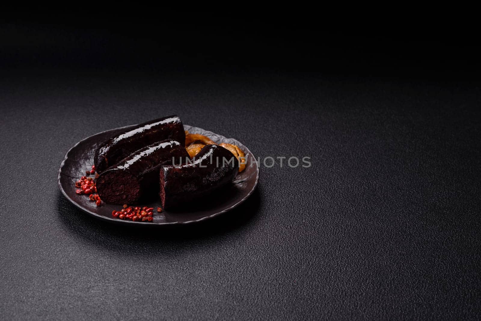 Delicious black blood sausage or black pudding with spices and herbs grilled on a black concrete background