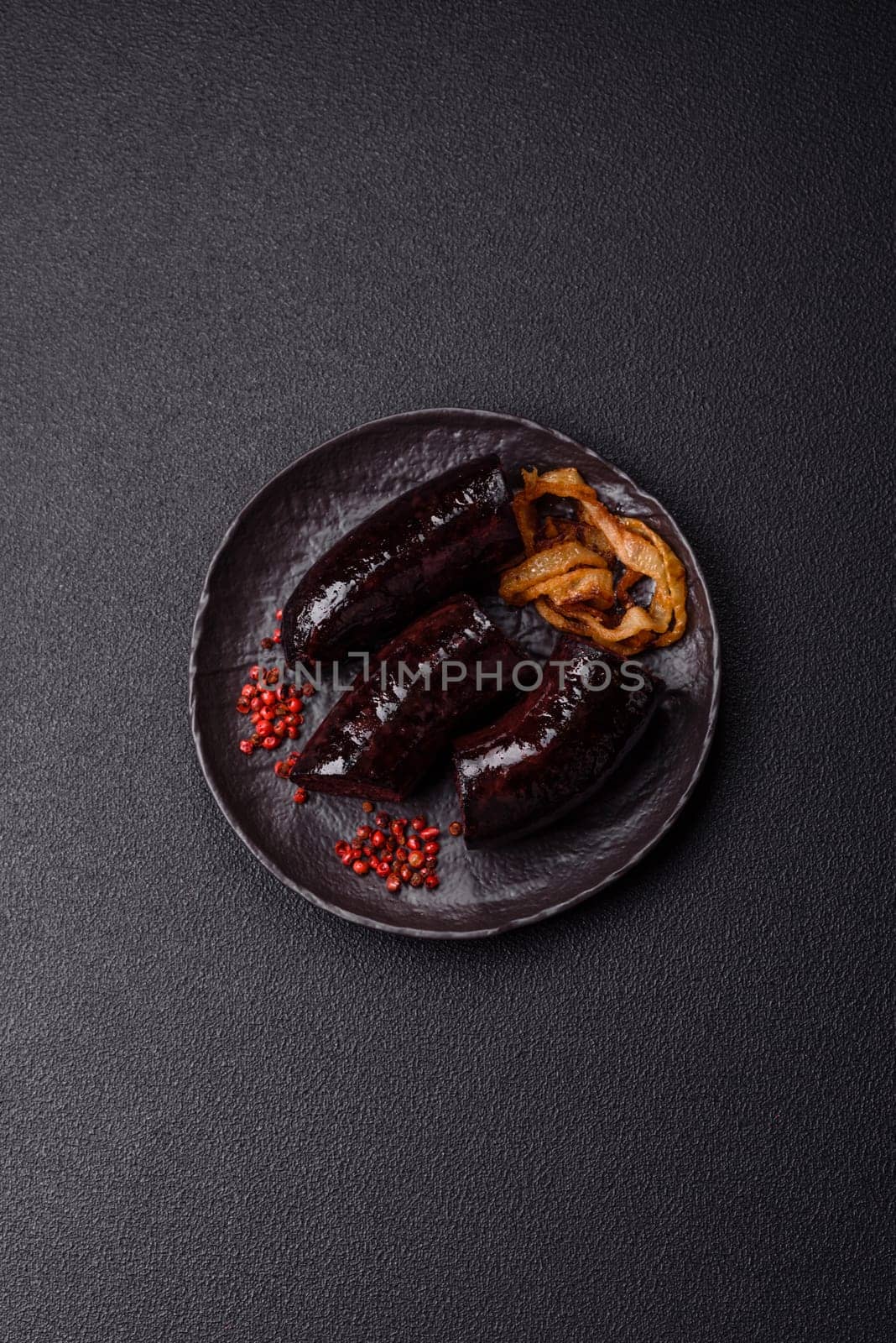 Delicious black blood sausage or black pudding with spices and herbs grilled on a black concrete background