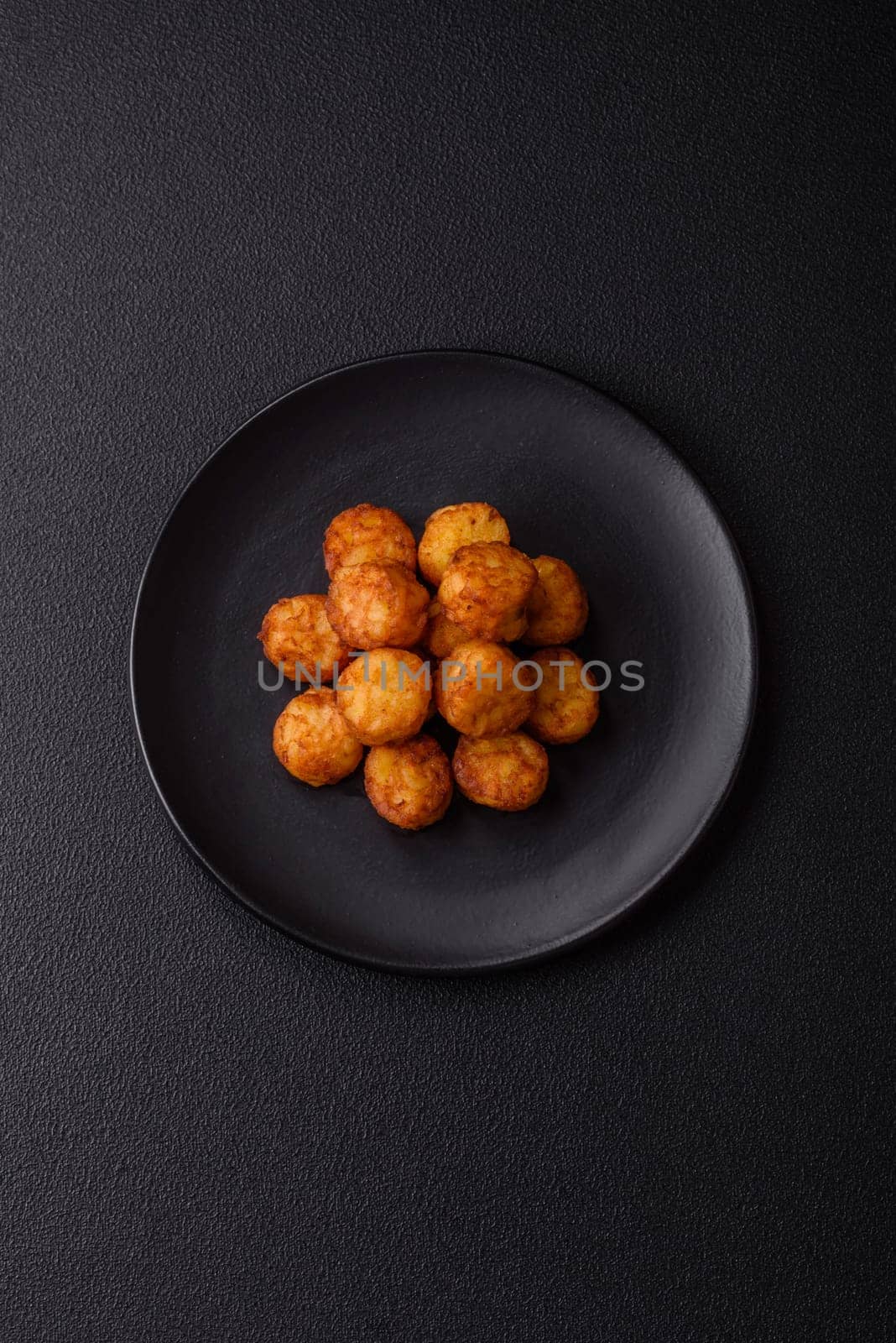 Delicious fried potato balls or croquettes with salt, spices and herbs on a dark concrete background