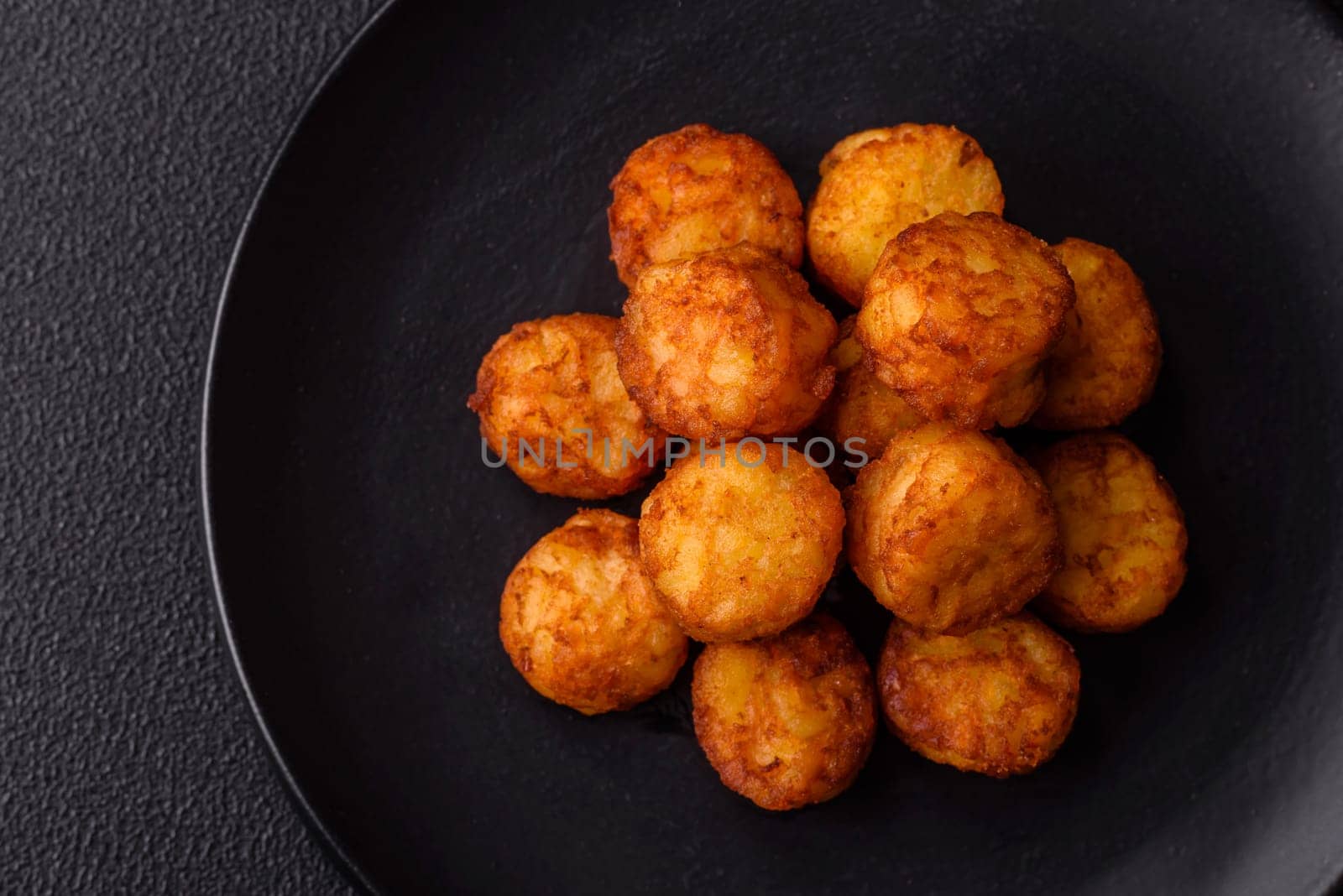 Delicious fried potato balls or croquettes with salt, spices and herbs on a dark concrete background
