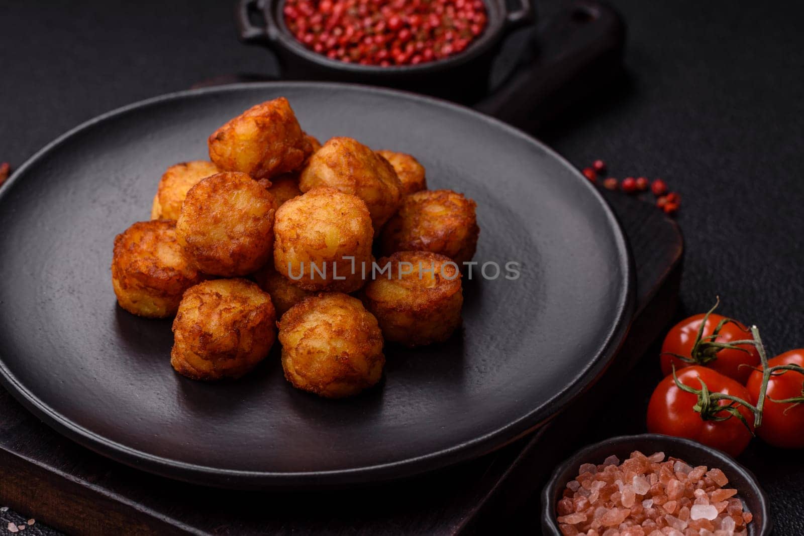 Delicious fried potato balls or croquettes with salt, spices and herbs on a dark concrete background