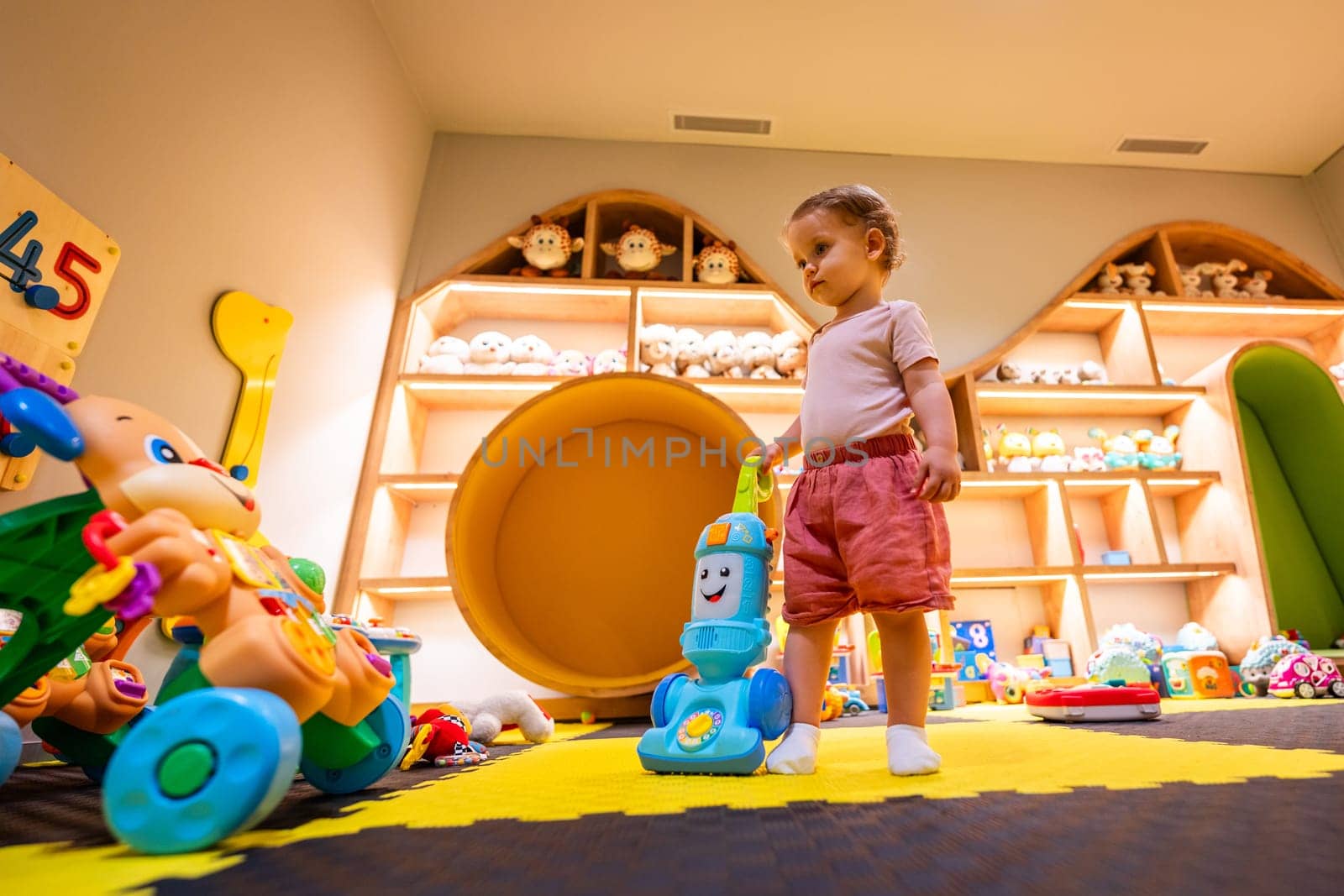 Child exploring with a toy vacuum cleaner in a vibrant and interactive play area for motor skills development